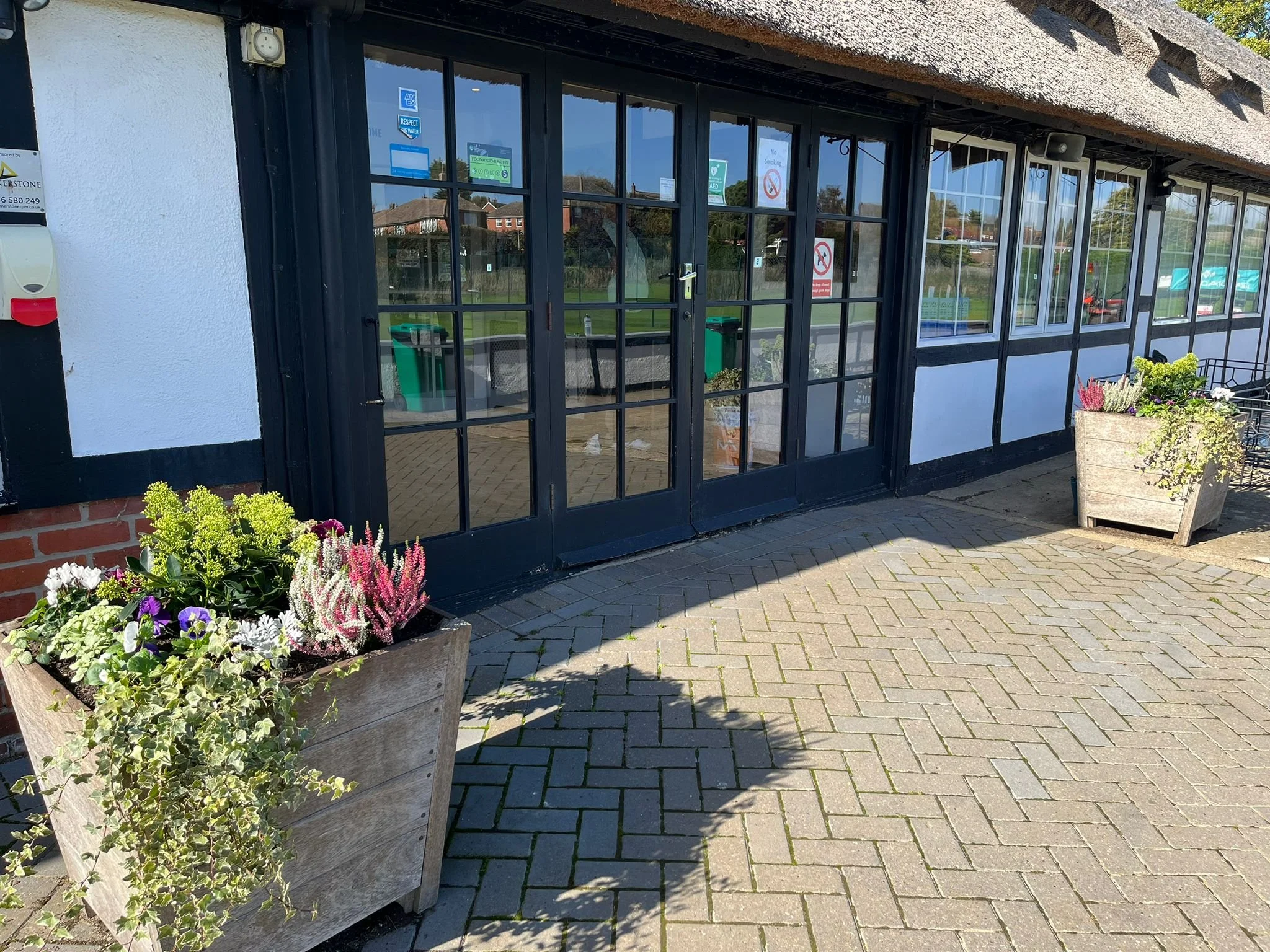 Outside view of a building with black framed glass doors and windows, potted flowers on either side, and a paved walkway.