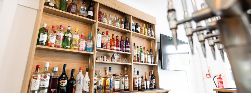 Wooden shelves filled with various bottles of liquor, with a television or monitor on the right and beer taps in the foreground.