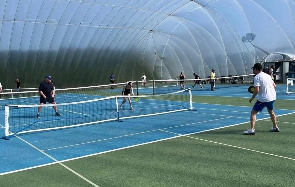People playing pickleball inside a large, glass-encased structure.