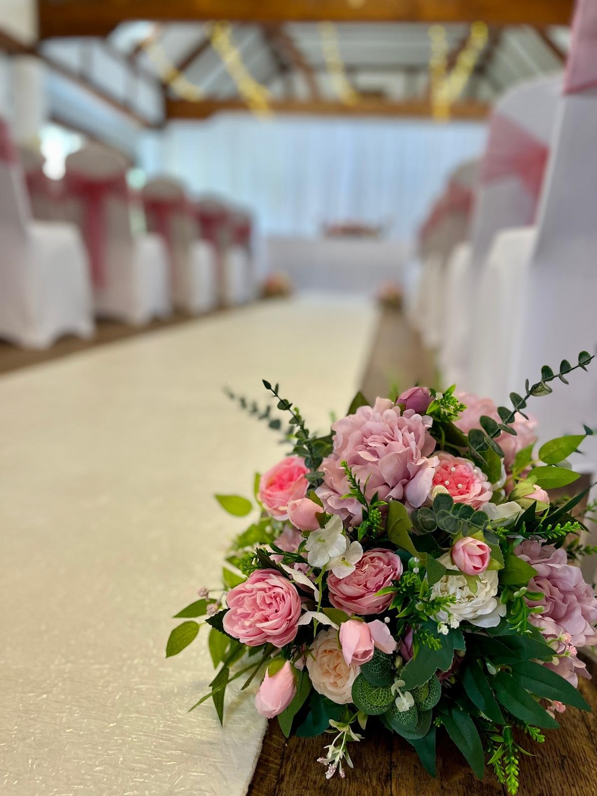 A bouquet of pink and white flowers with green leaves placed on a table at a decorated event venue.