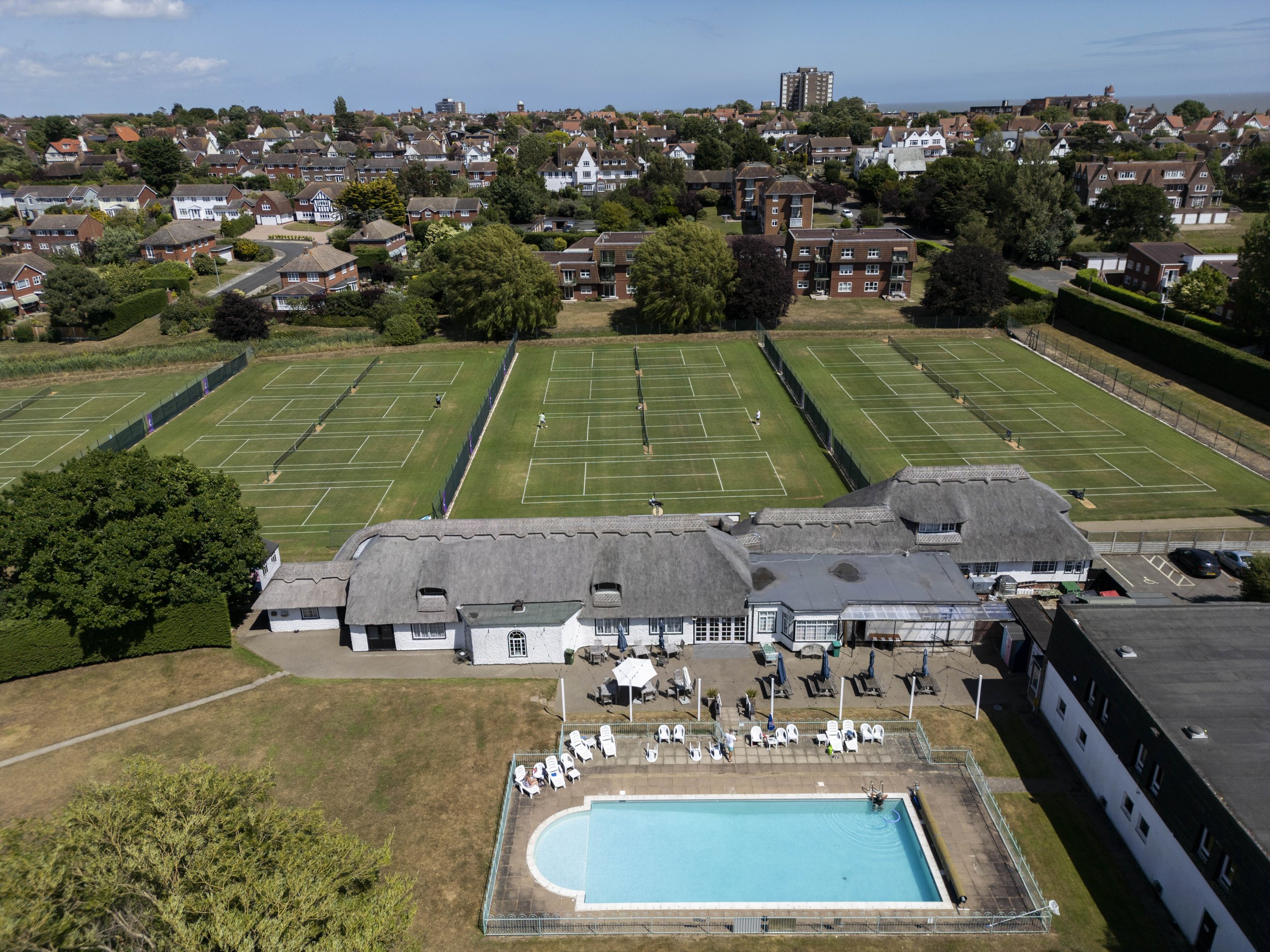 Aerial view of tennis courts, a swimming pool, and surrounding residential buildings in a neighborhood.