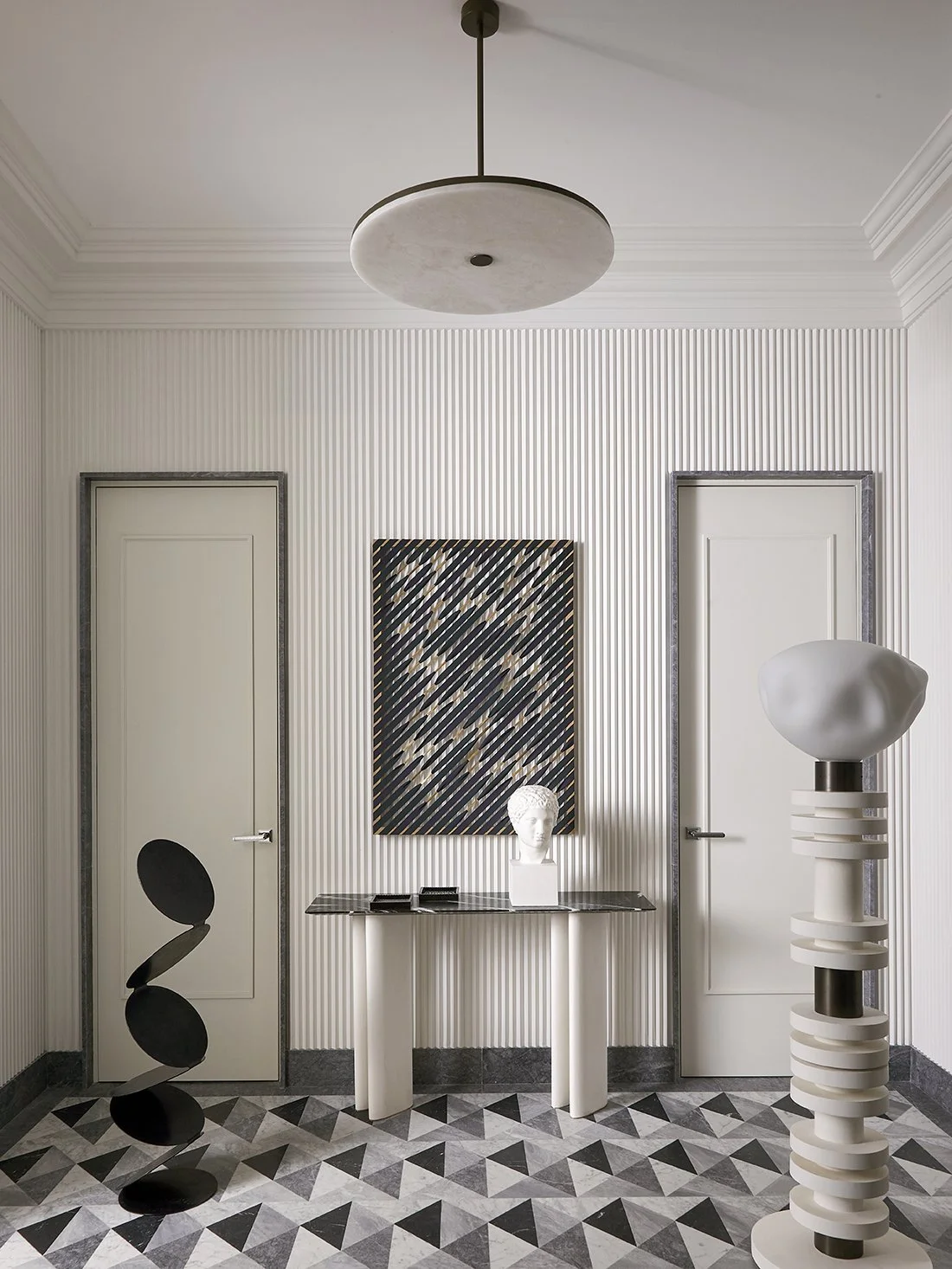 Intérieur d'une pièce élégante avec décoration moderne, deux portes blanches, un tableau abstrait, une sculpture en forme de tête et une sculpture en spirale blanche.