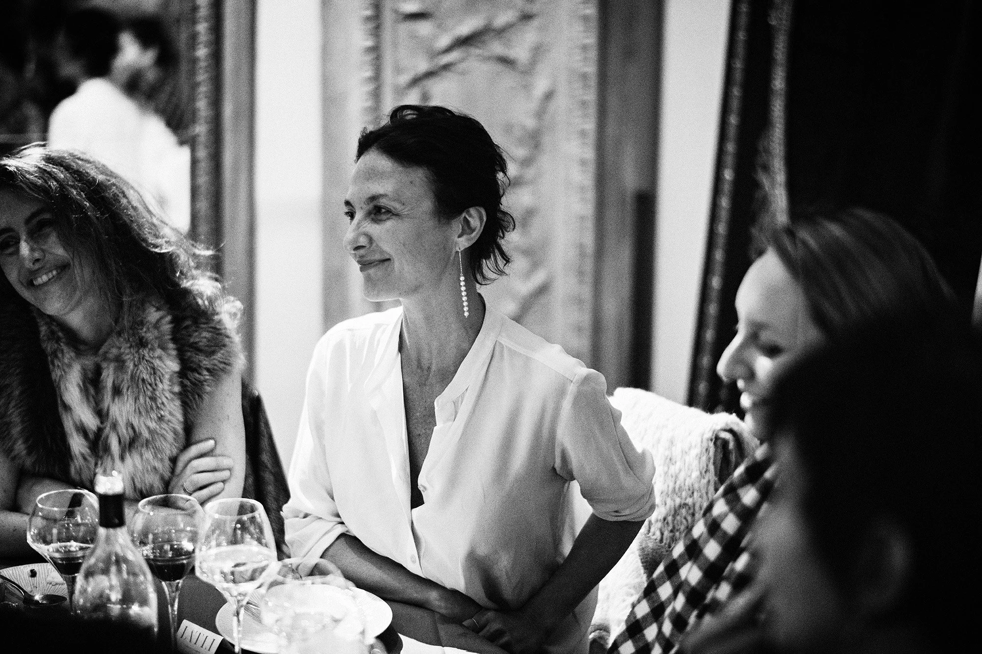 Groupe de femmes assises autour d'une table lors d'un dîner, souriantes, dans une pièce élégante.