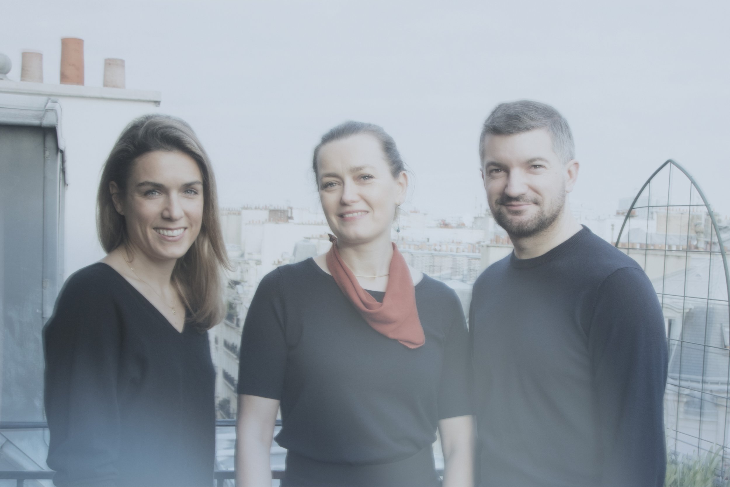 Trois personnes posant sur un toit avec une vue sur la ville en arrière-plan.