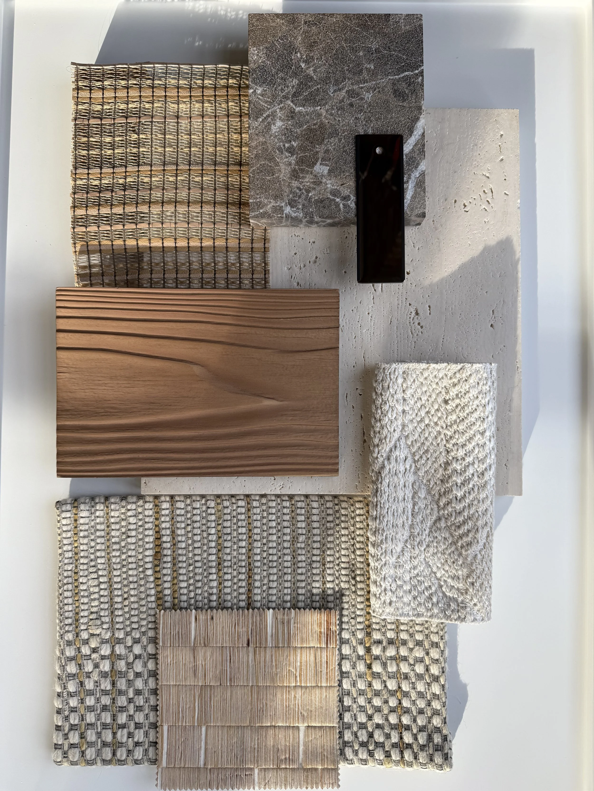 Différents échantillons de matériaux pour décoration intérieure, y compris du bois, de la pierre, du tissu tissé, du céramique, et un tapis, disposés sur une surface blanche