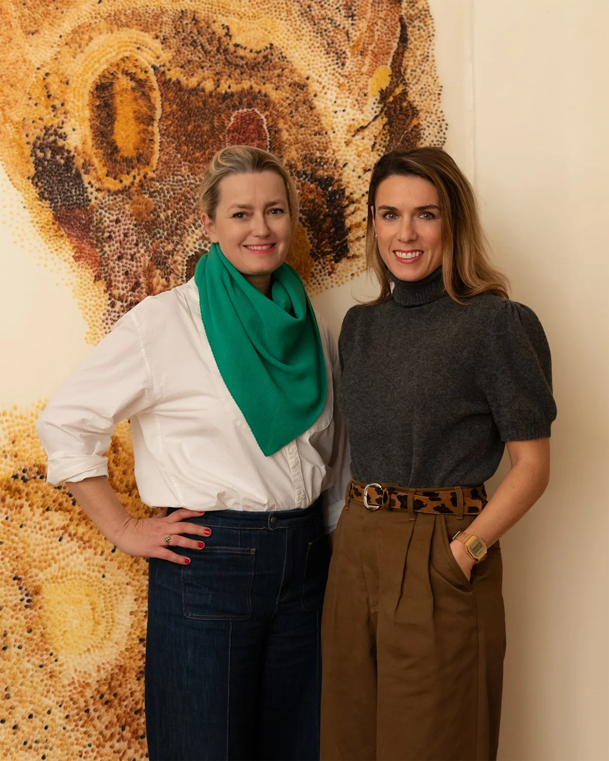 Deux femmes posent devant une œuvre d'art abstraite composée de petits points de couleur variant du jaune au brun.