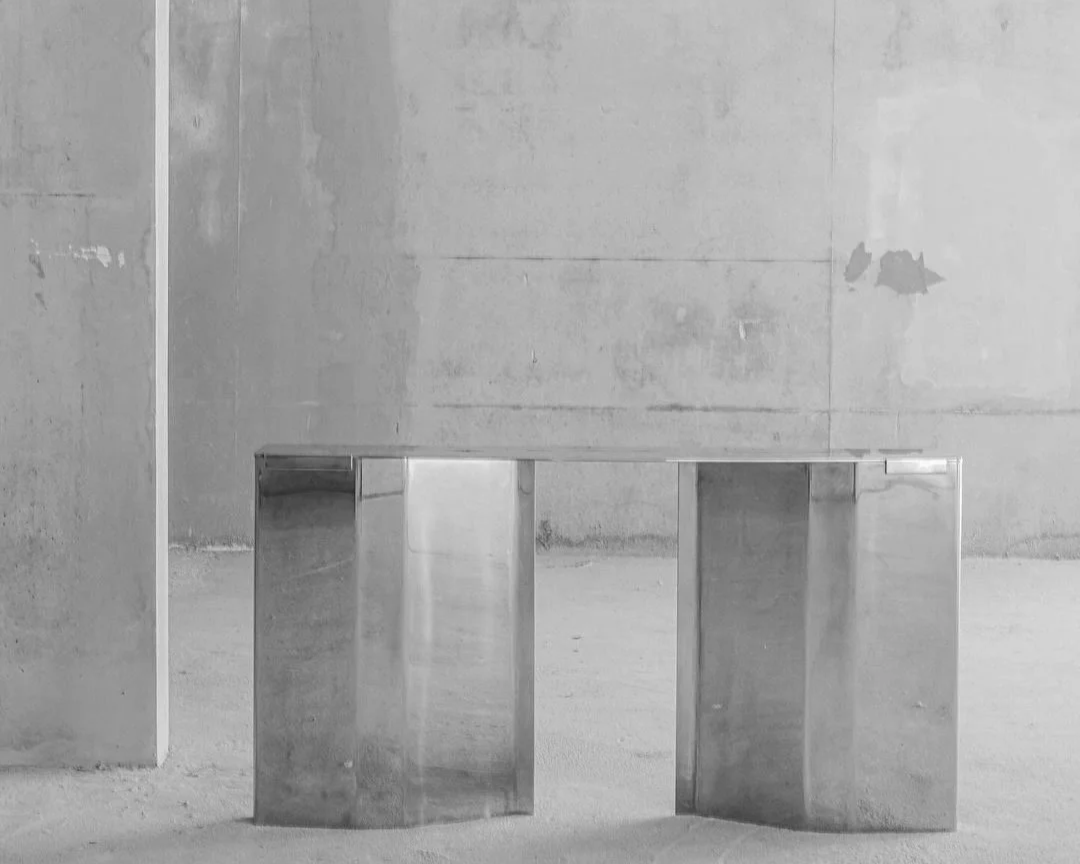 A minimalist metallic bench in an industrial space with concrete walls and floor.