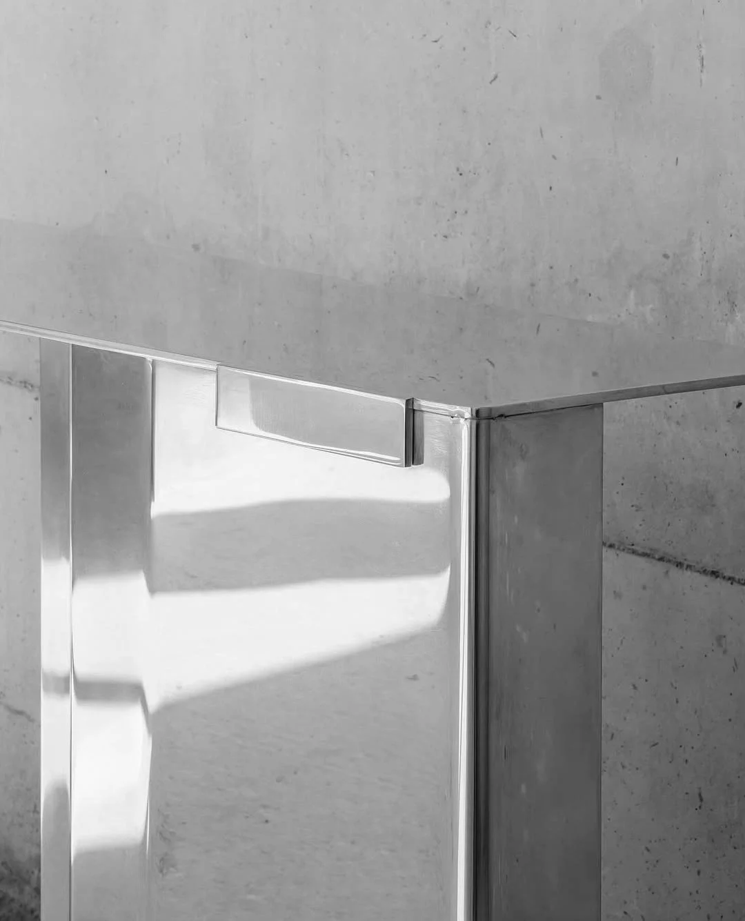 Close-up of a stainless steel door with a handle, set against a concrete wall.