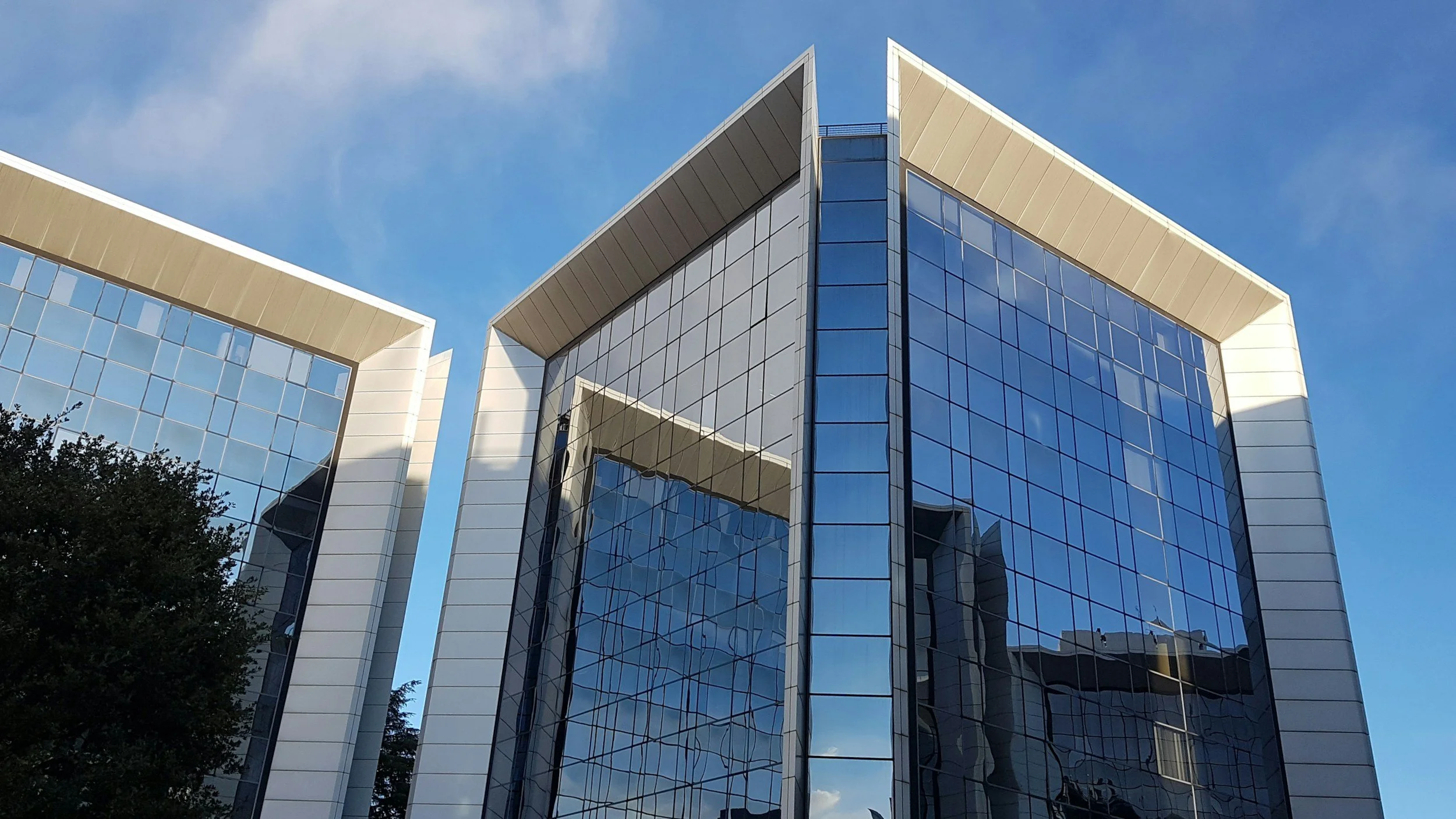 A modern glass office building with reflective windows against a blue sky.