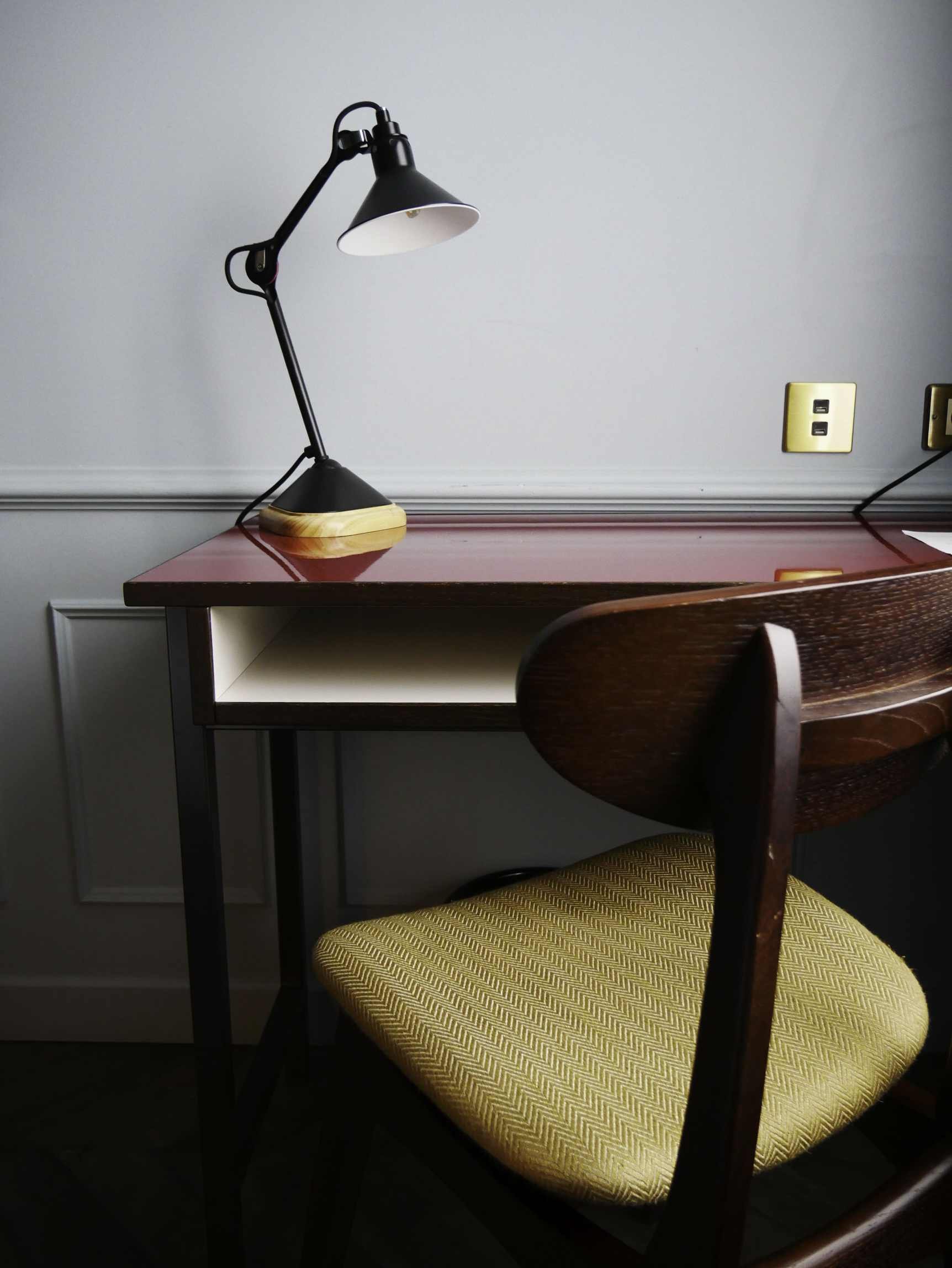 Un bureau avec une lampe de bureau noire, une chaise avec un coussin jaune à motif herringbone, une prise électrique murale. Photo professionnelle prise dans le cadre d'un reportage photo dans un hotel.