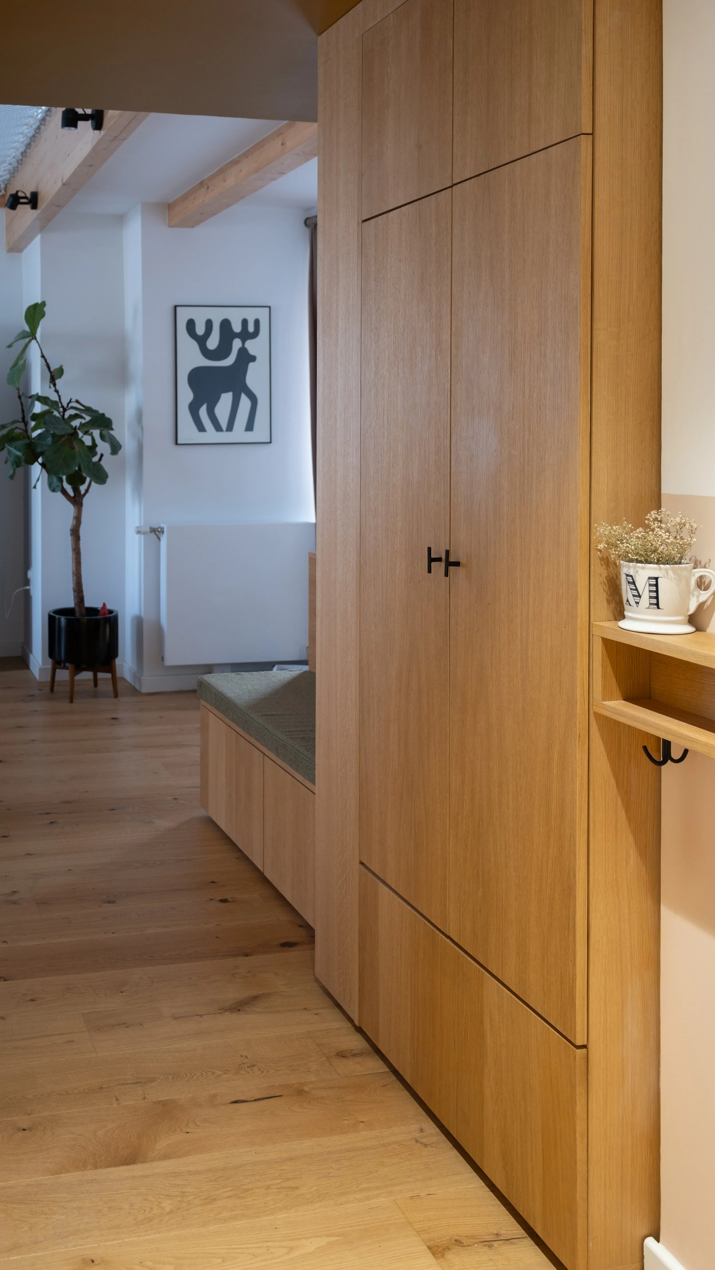 Intérieur d'une maison avec un meuble en bois, une plante verte, un tableau avec un cerf stylisé, et une étagère décorative.