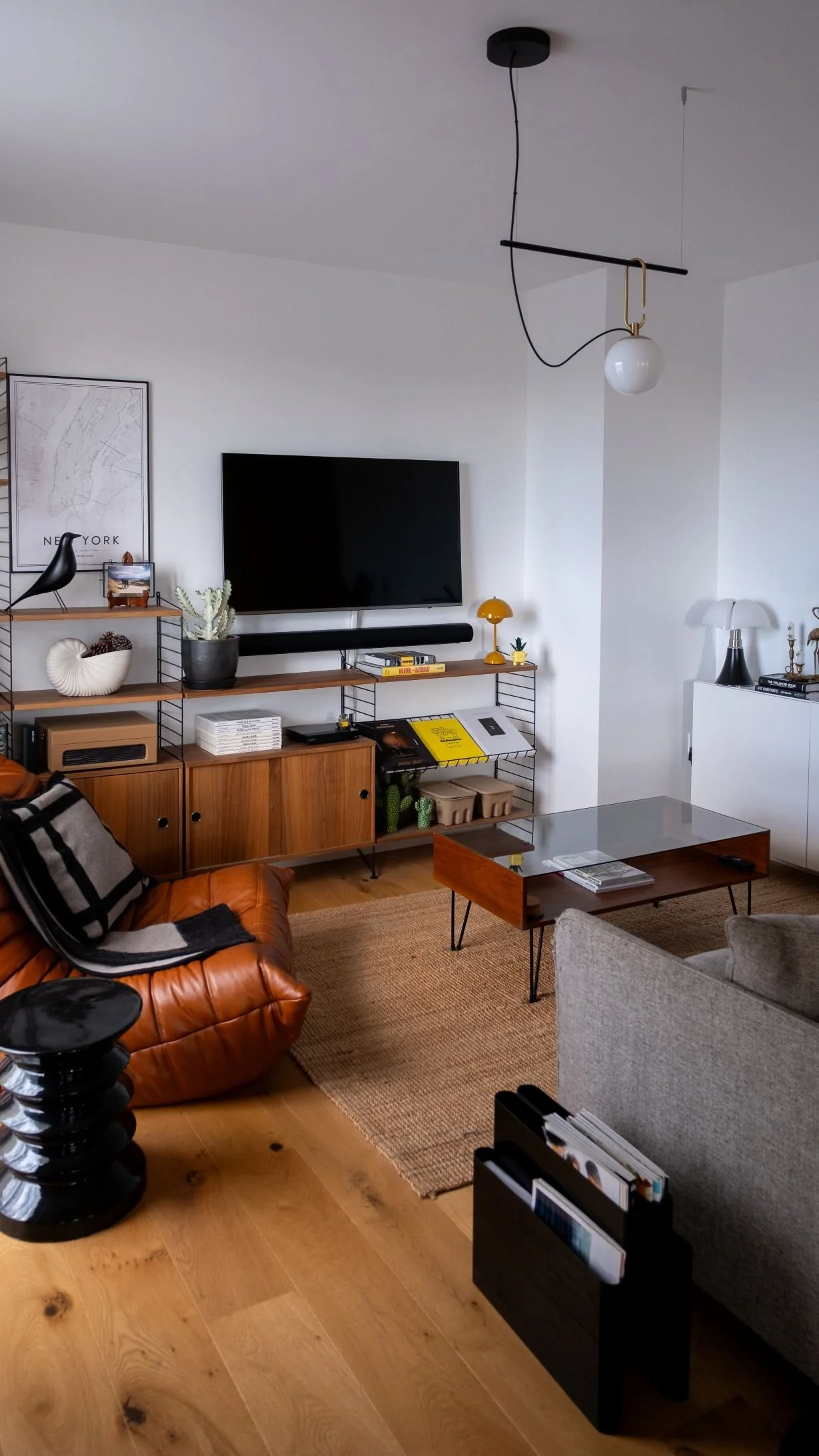 Salon moderne avec un meuble en bois, un canapé en cuir marron Togo ligne roset, un tapis en jute, une télévision murale, et des décorations comme des plantes, des lampes et des cadres. Reportage photo immobilière pour agent immobilier à Bordeaux