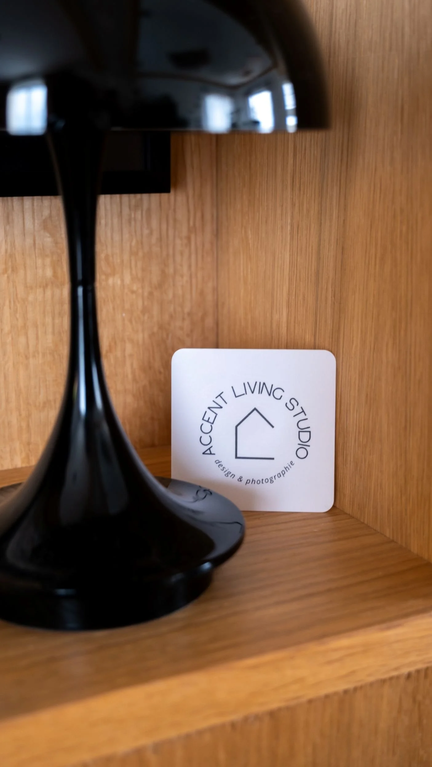 Une lampe portable Louis Poulsen noire, une carte de visite pour Accent Living Studio, en bois naturel. Présentation d'un meuble d'entrée sur mesure en bois.