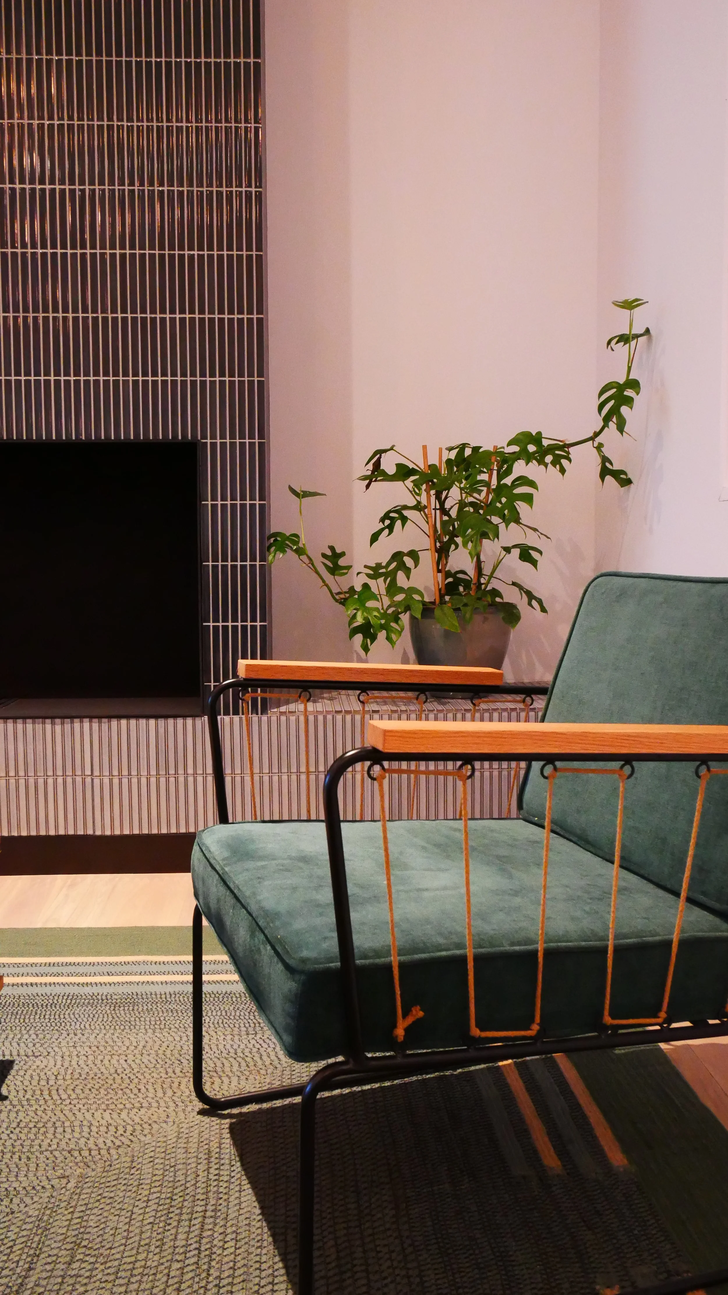 Un coin salon avec un fauteuil vert, une plante verte en pot sur une table, un mur avec des carreaux noirs et blancs, et un tapis en dessous.