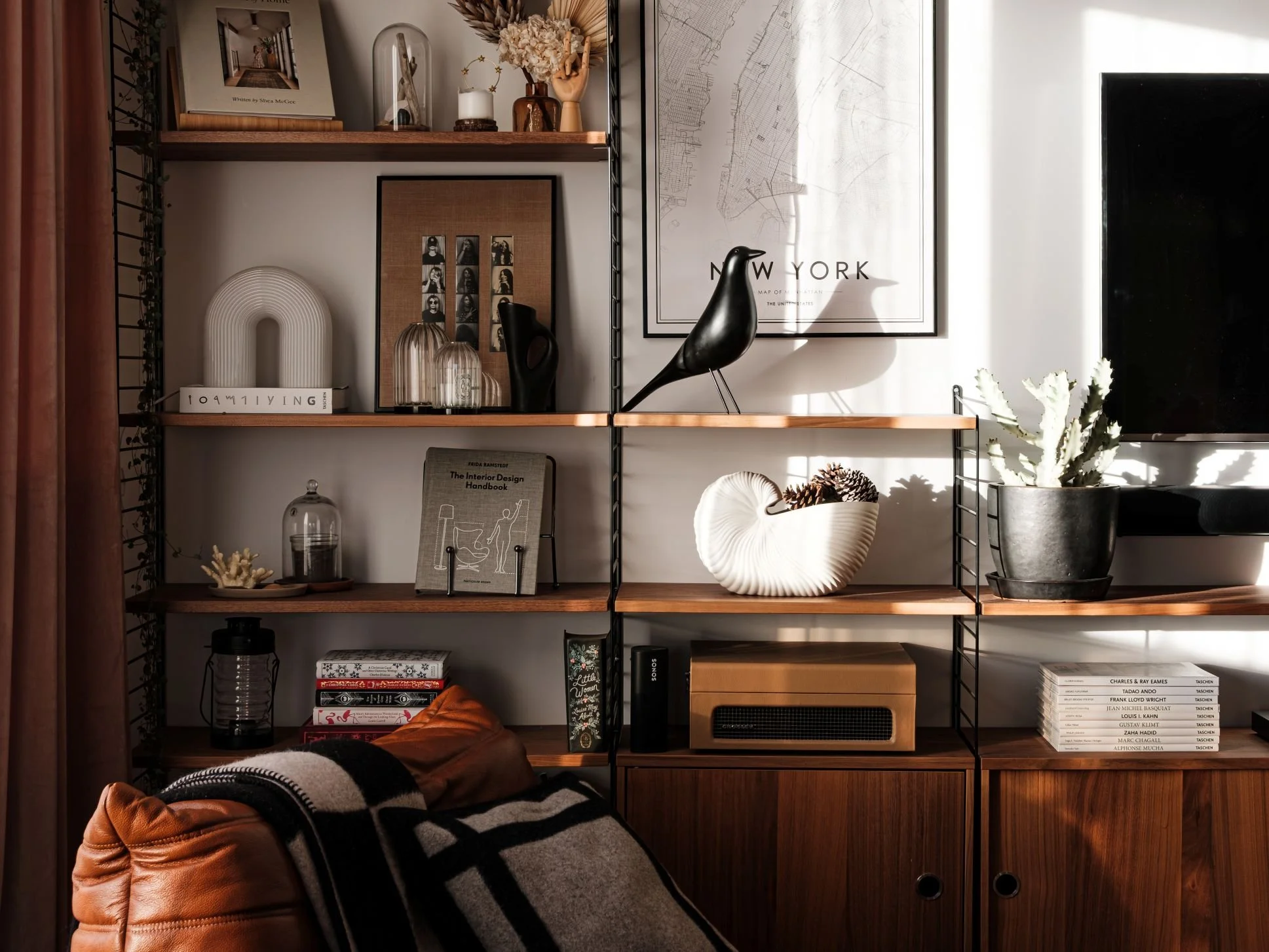 Étagère murale en bois noyer String Furniture avec décorations et livres, dont une plante grasse en pot, un oiseau eames House bird Vitra en sculpture bois noire, des cadres et des livres