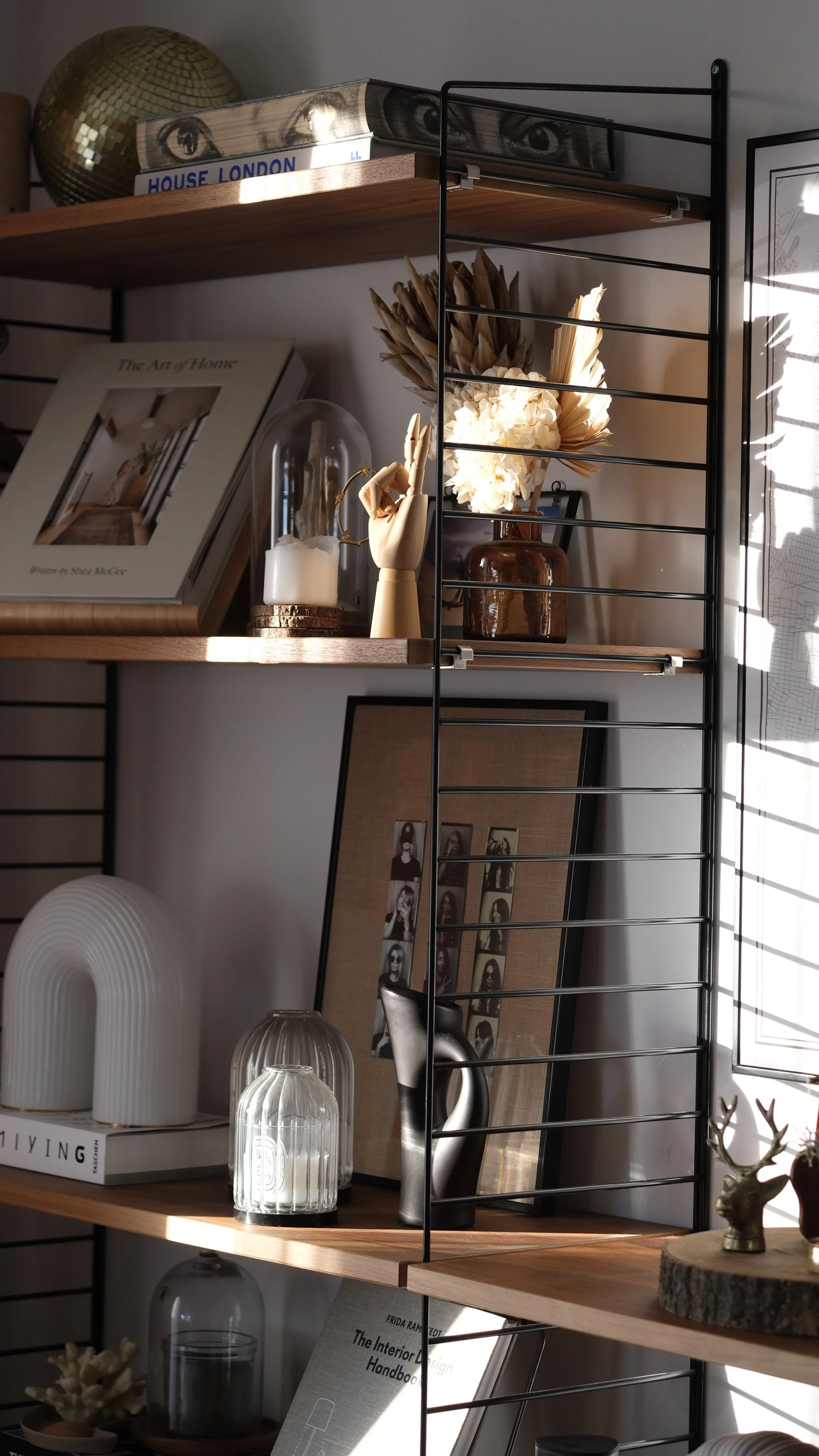 Étagère murale avec des décorations, des livres et des objets décoratifs, éclairée par la lumière naturelle.