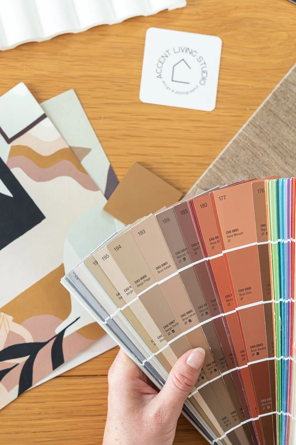 Nuancier de couleurs de peinture avec différentes teintes et codes, posé sur une table en bois, avec des échantillons de matériaux et un tag indiquant 'Accent Living Studio'.