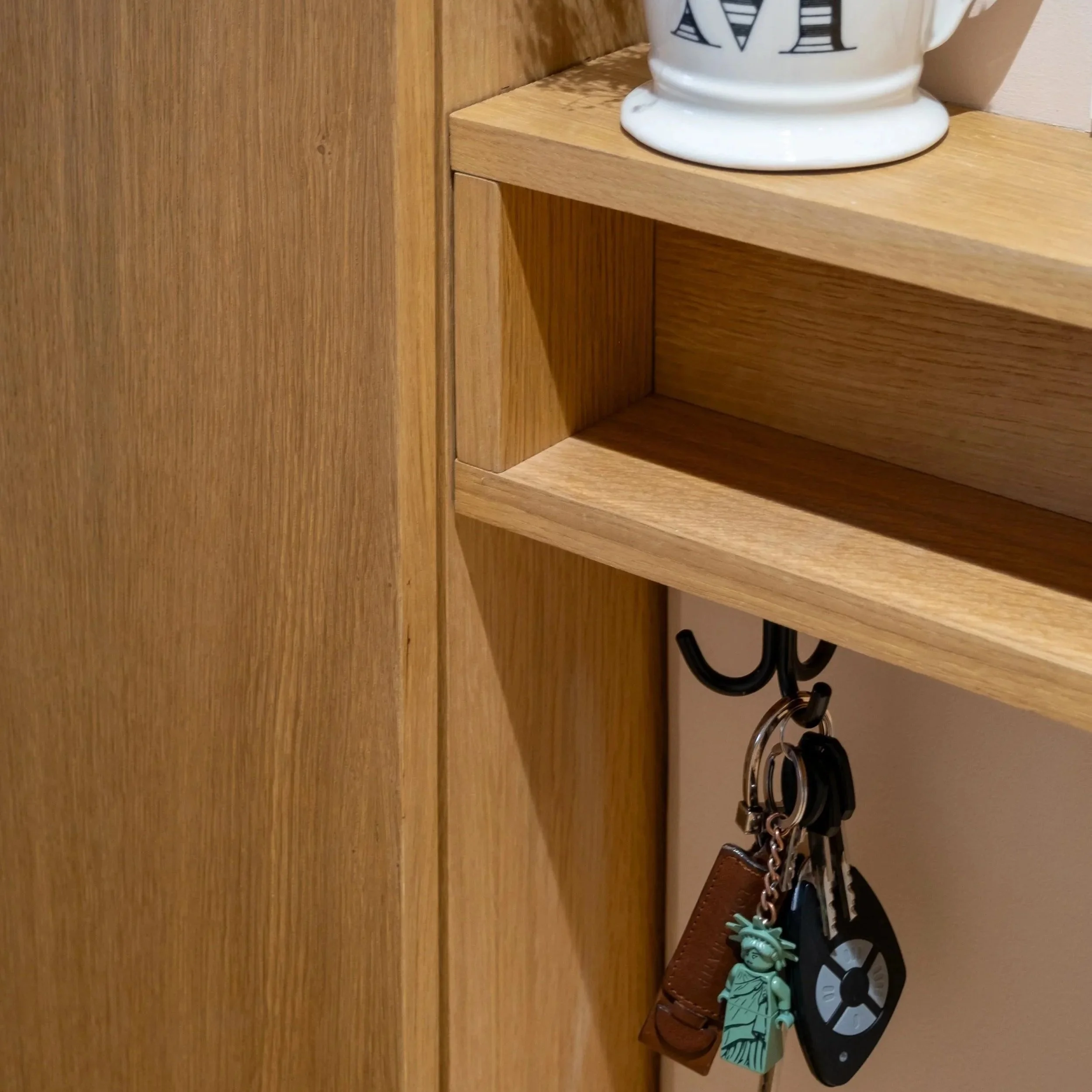 Détail d'un meuble d'entrée sur mesure réalisé à Bordeaux par une décoratrice d'intérieure, Accent Living Studio, crochet pour clé avec porte-clés, porte-clés avec un figurine, portant un casque, et un porte-clés en forme de Statue de la Liberté