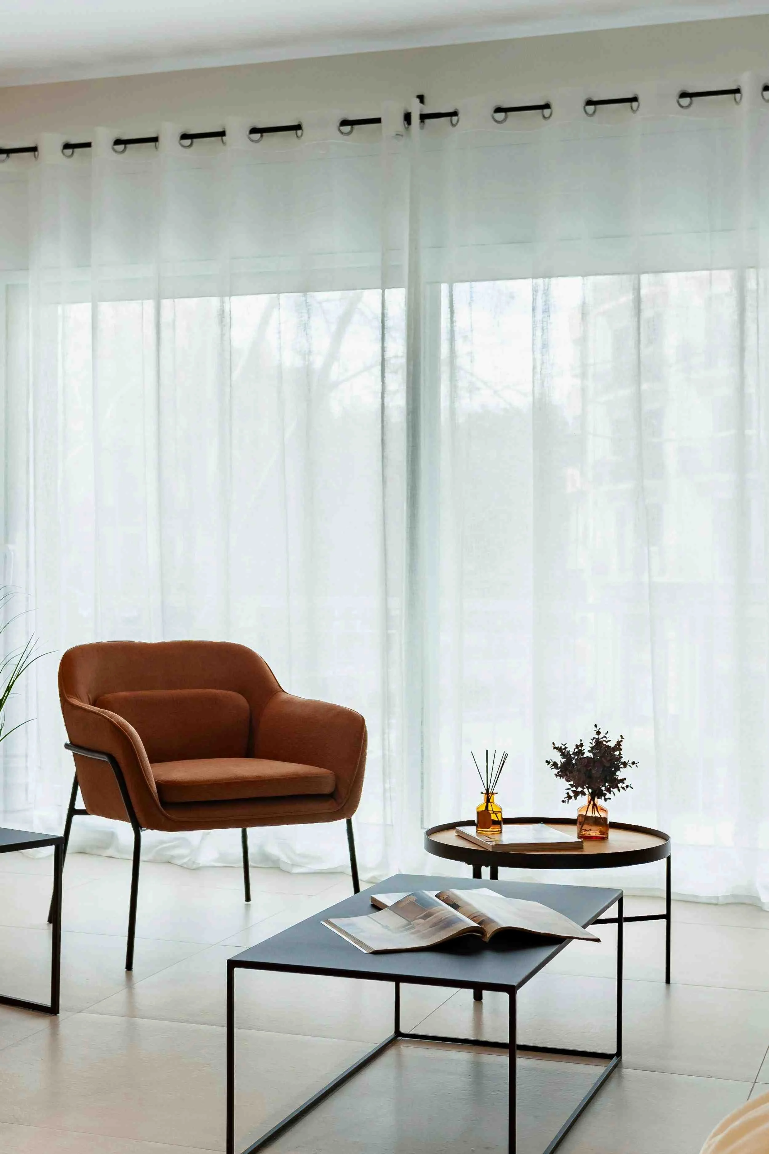 Salon moderne avec un fauteuil en cuir marron, une table basse avec des magazines ouverts, et des fleurs dans des vases en verre. Proposition de décoration d'un appartement témoin pour promoteur ou agent immobilier à Bordeaux