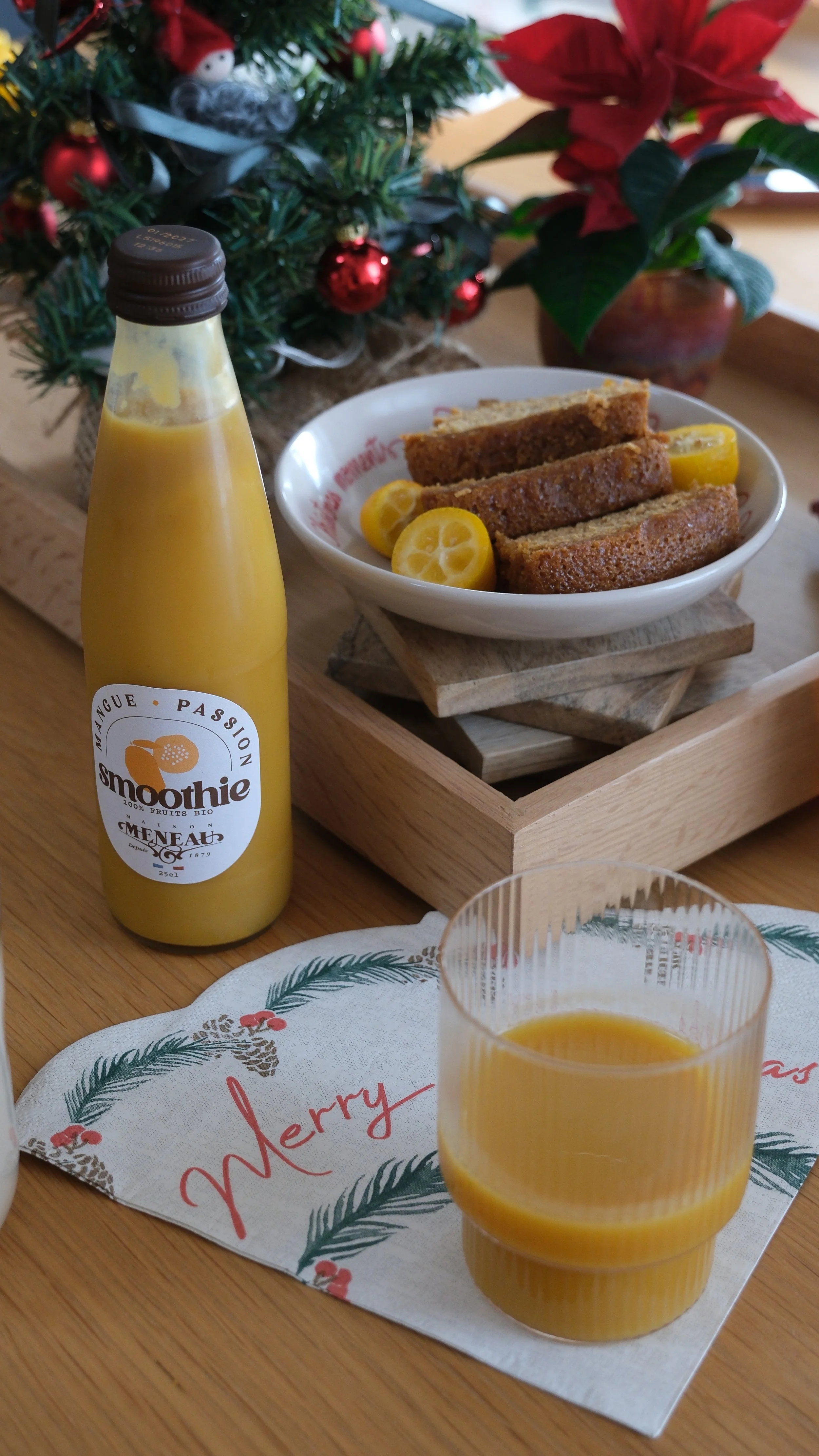 Verrre de jus d'orange, assiette avec des tranches de gâteau et des quartiers de kumquats, décorations de Noël avec un sapin étoilé et une poinsettia.