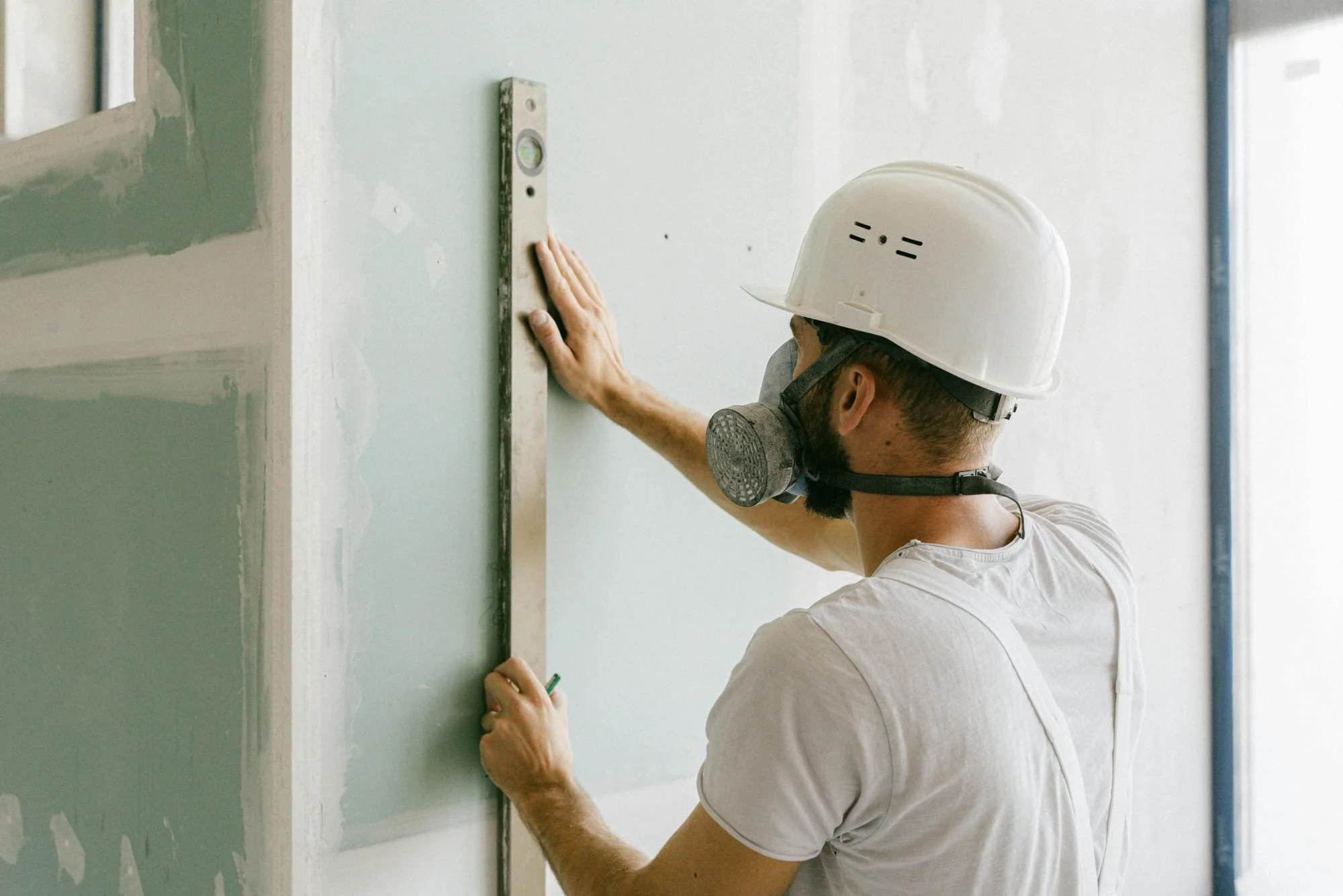 Un homme portant un casque de sécurité et utilise une règle pour faire des marquages sur un mur en construction. Photo illustrant un reportage photo professionnel de chantier