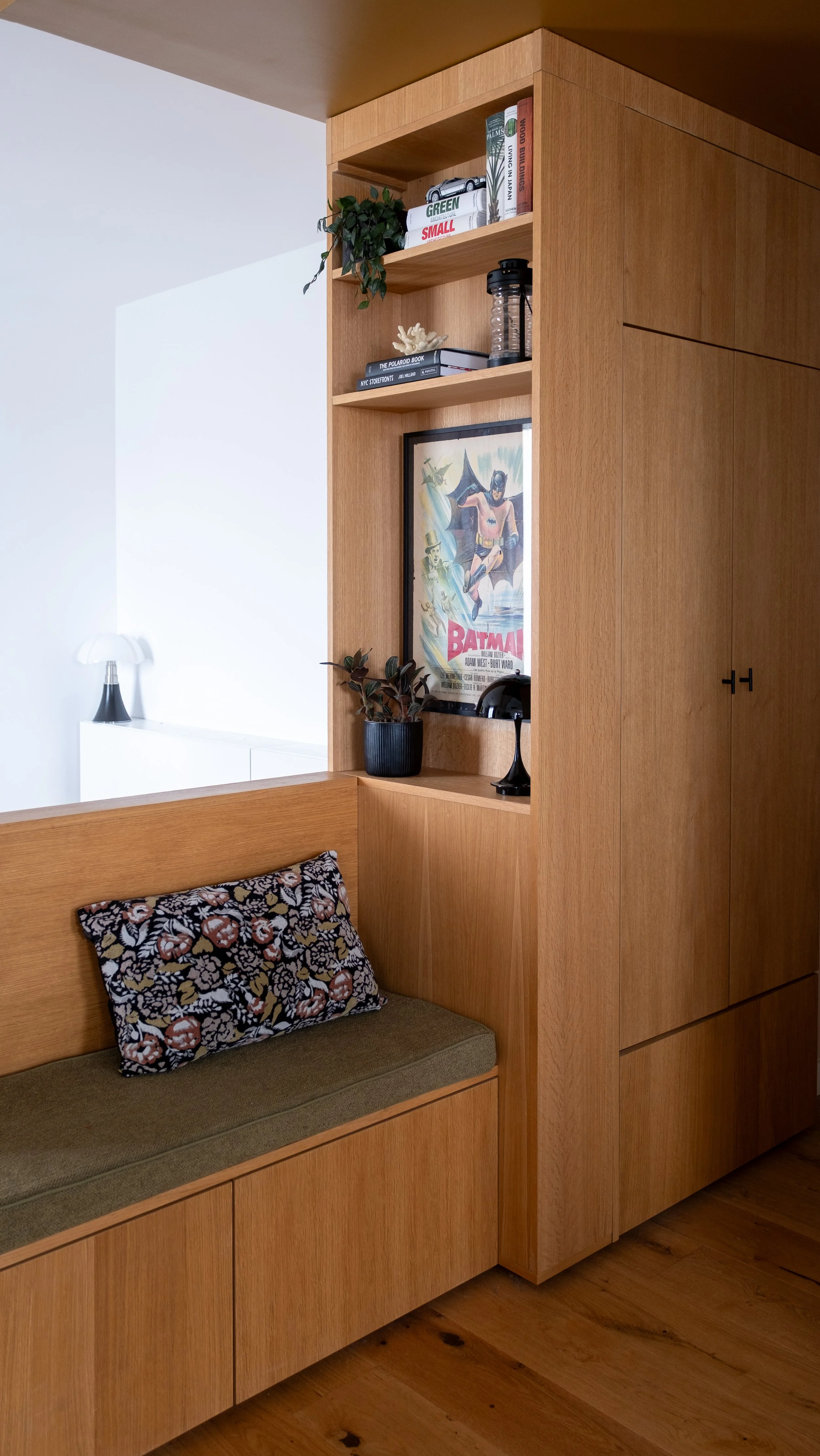 Un meuble en bois avec des étagères, un cadre avec une affiche vintage de Batman, une plante et divers objets decoratifs.