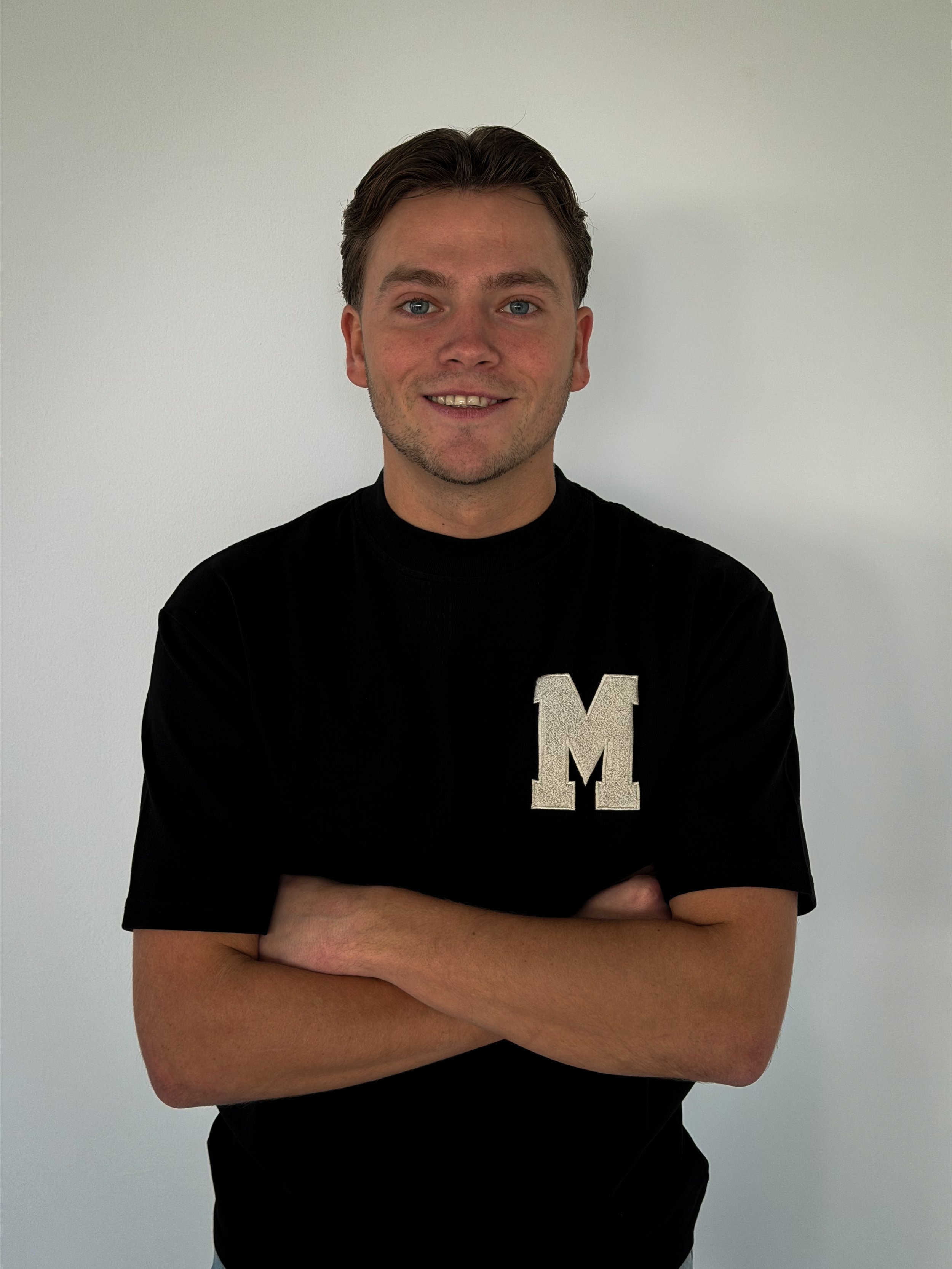 A smiling woman with curly afro hair wearing glasses, hoop earrings, layered necklaces, and a striped shirt.