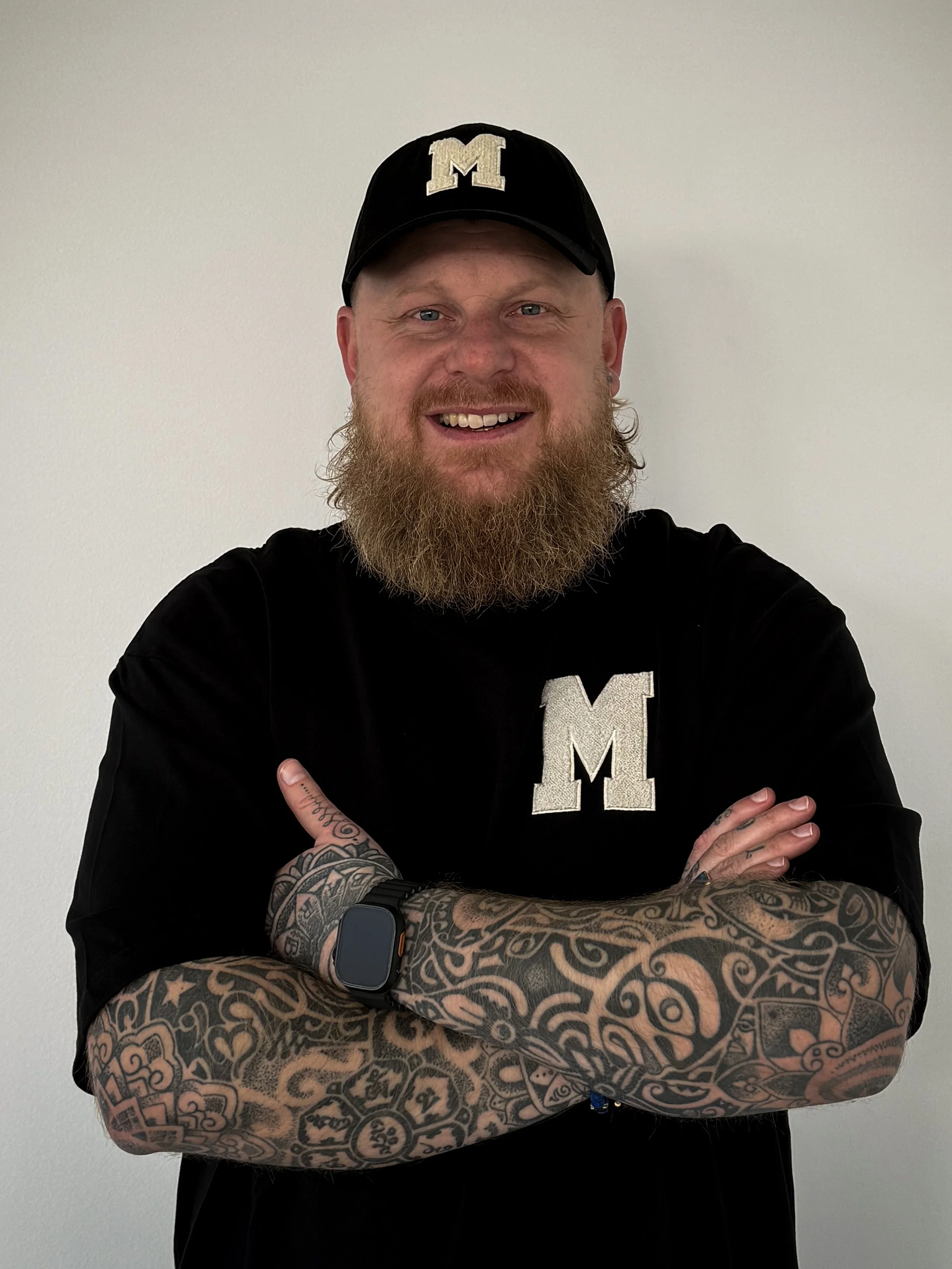 A man with glasses and a beard sitting indoors, looking slightly to the side.