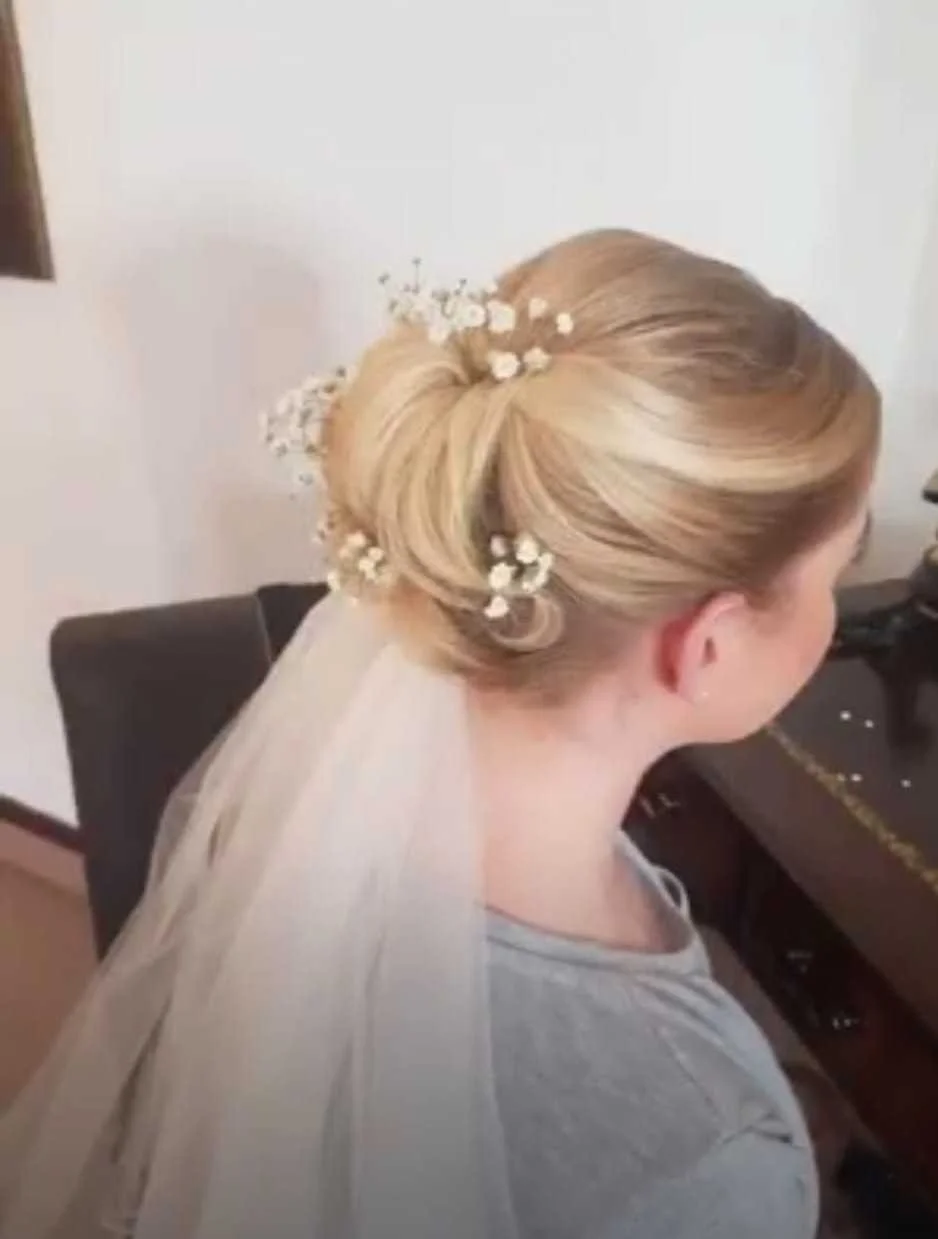 Brunette woman with styled blonde hair adorned with white baby’s breath flowers, wearing a wedding veil, sitting at a piano.