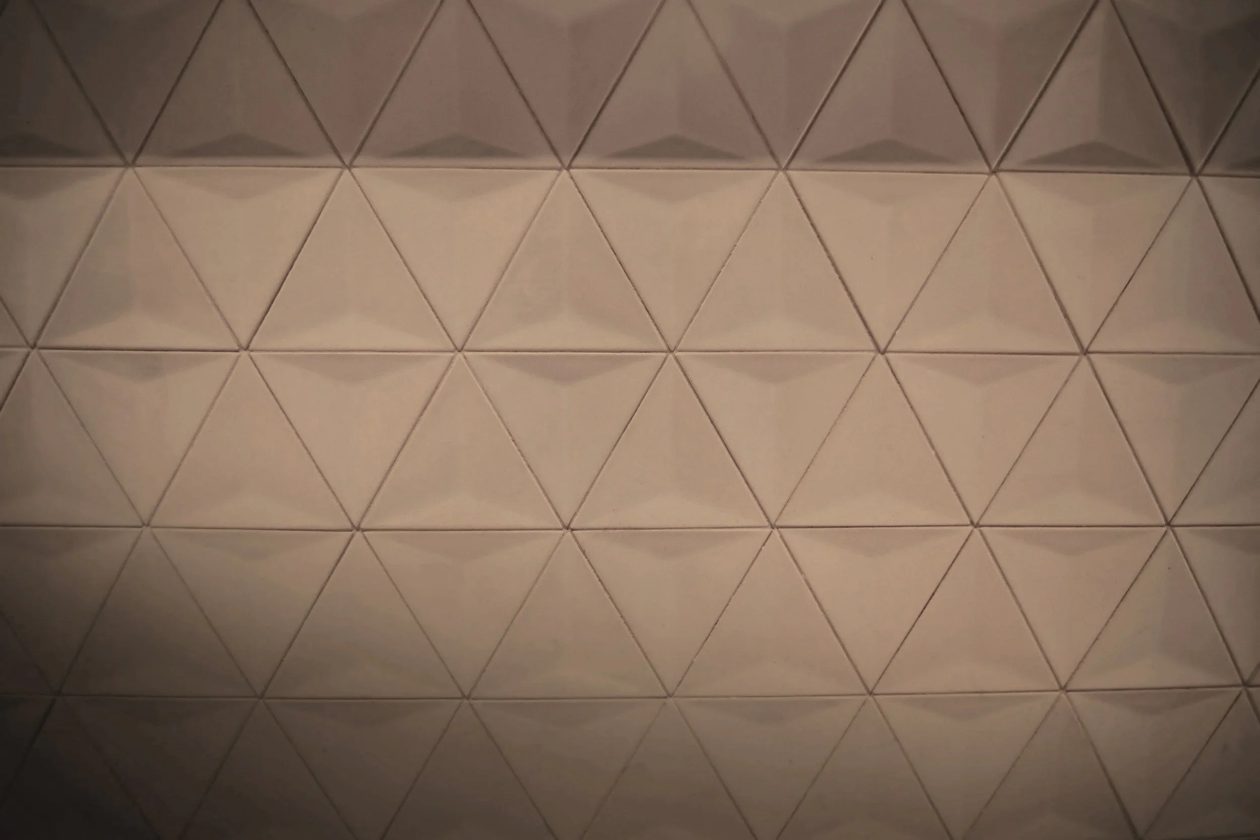Close-up of a wall covered in triangular tiles arranged in a repeating pattern with subtle shadows.