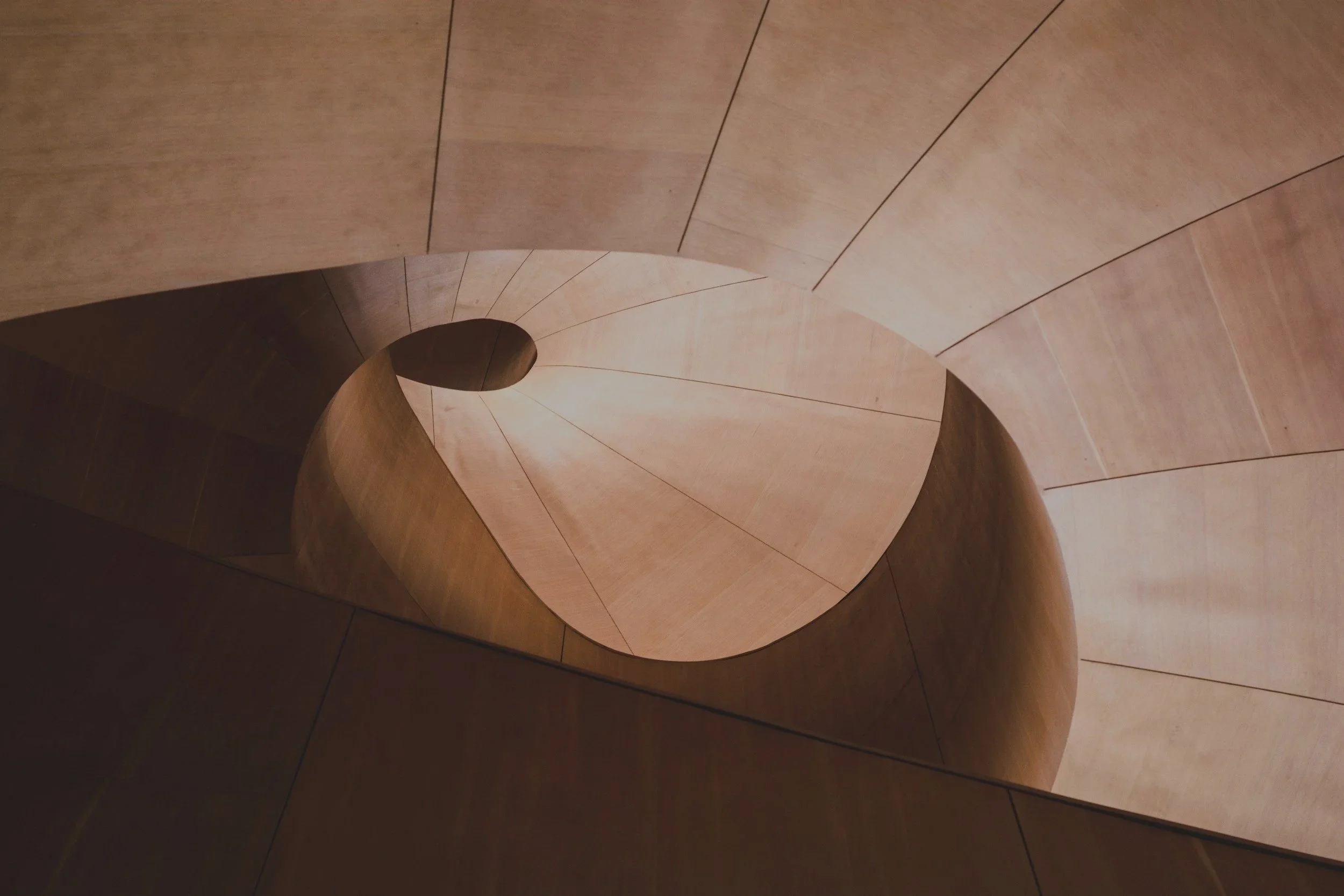 A spiral staircase with wooden steps viewed from below, creating a swirling pattern.
