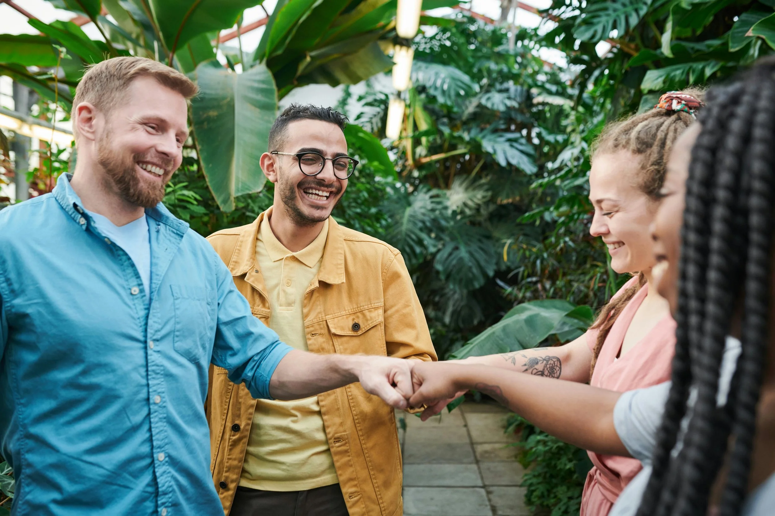 Group of diverse people in a greenhouse, smiling, shaking hands, and greeting each other.