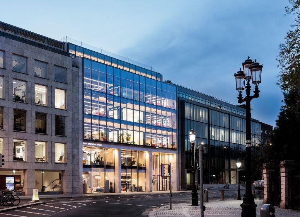 The Completed No. 70 St. Stephens Green modern office building with glass exterior, illuminated from inside, located at teh corner of St. Stephens Green South and Earlsfort Terrace with street lamps and parked bicycles.