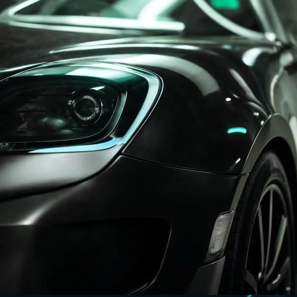 Close-up of a black sports car's front left headlight and wheel, with reflections on the shiny surface.