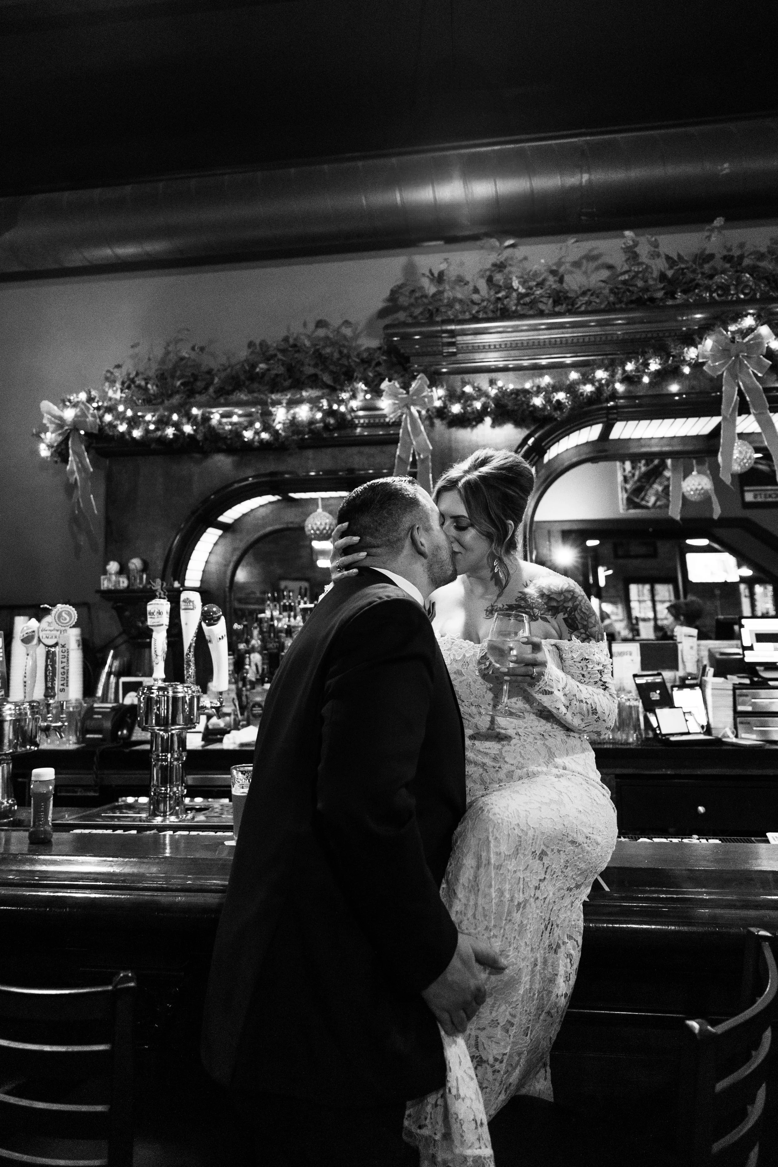 A couple kissing at a bar during a celebration, with Christmas decorations and garlands.