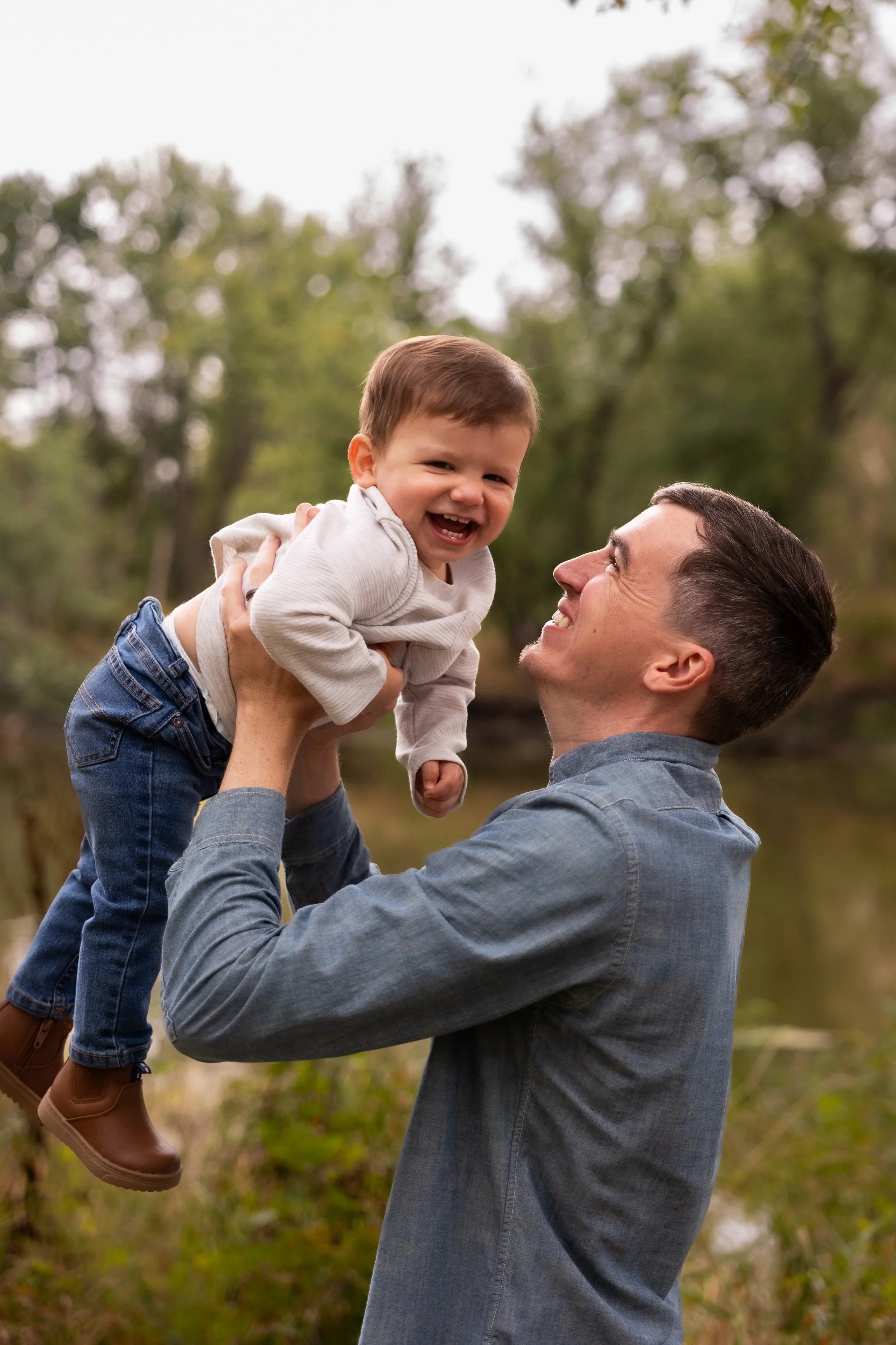 A man lifting a young boy in an outdoor setting with trees in the background, both smiling and enjoying the moment.