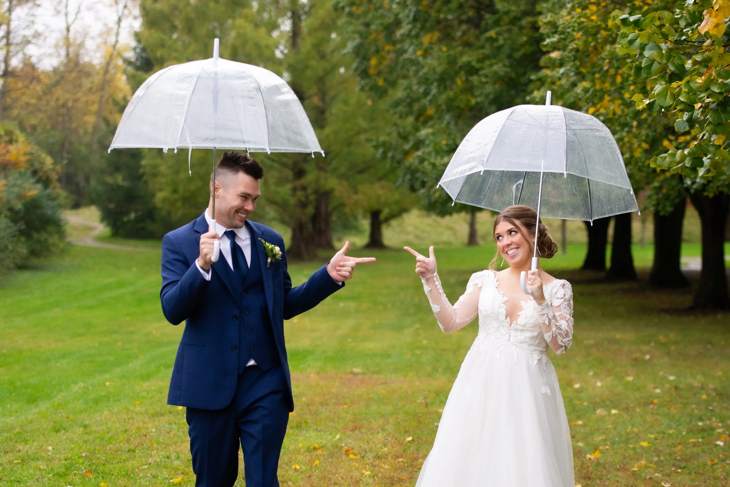 A couple holding a wedding bouquet of white and pink roses, greenery, and other flowers, with the man wearing a suit and watch, and the woman in a white dress and jewelry.