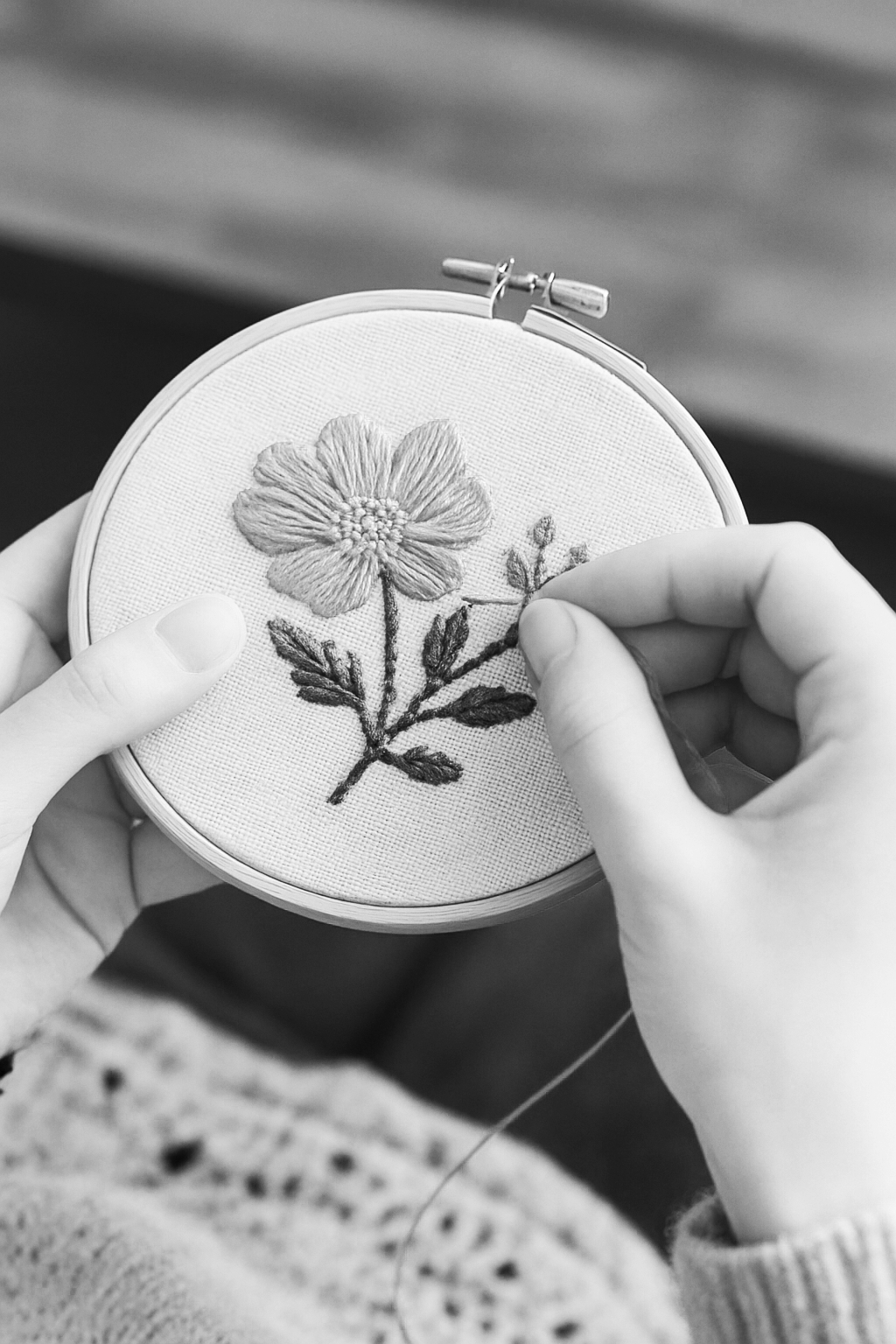 Close-up of hands embroiderying a flower on fabric in an embroidery hoop.