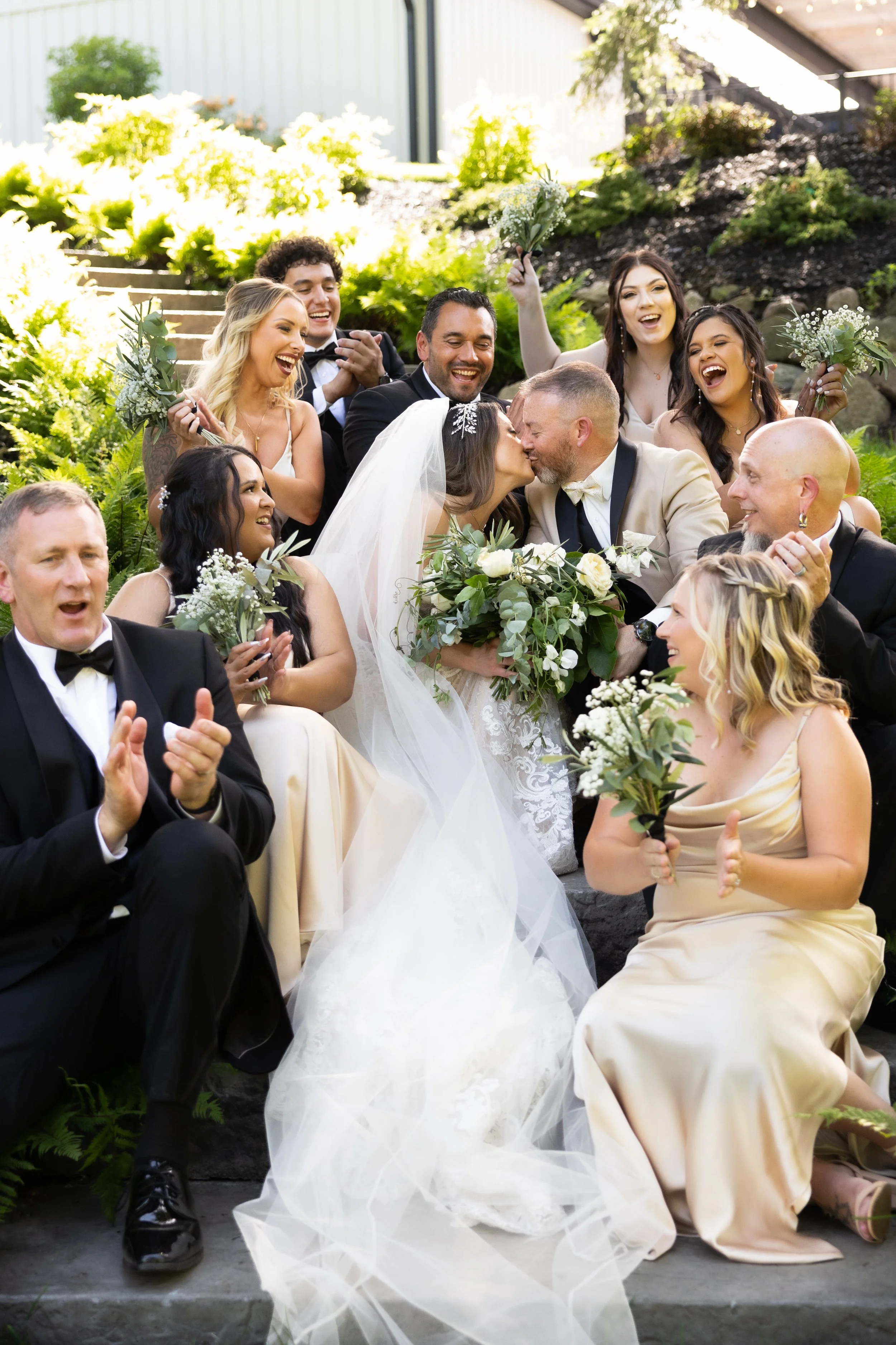 A bride and groom sitting together on a boat during sunset, with the bride dressed in a lace wedding gown and the groom in a black suit, on a body of water with trees in the background.