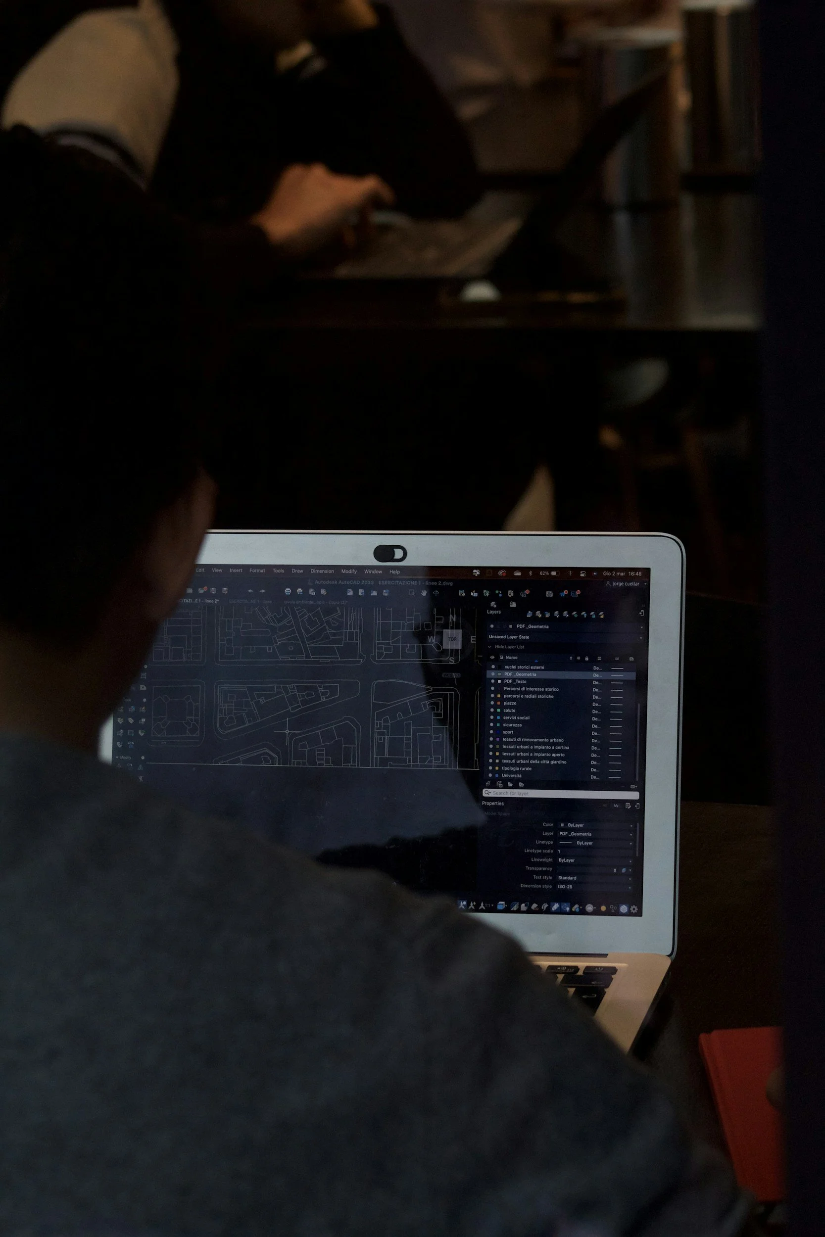 Person working on a laptop with a map or architectural drawing on the screen, in a dimly lit room.