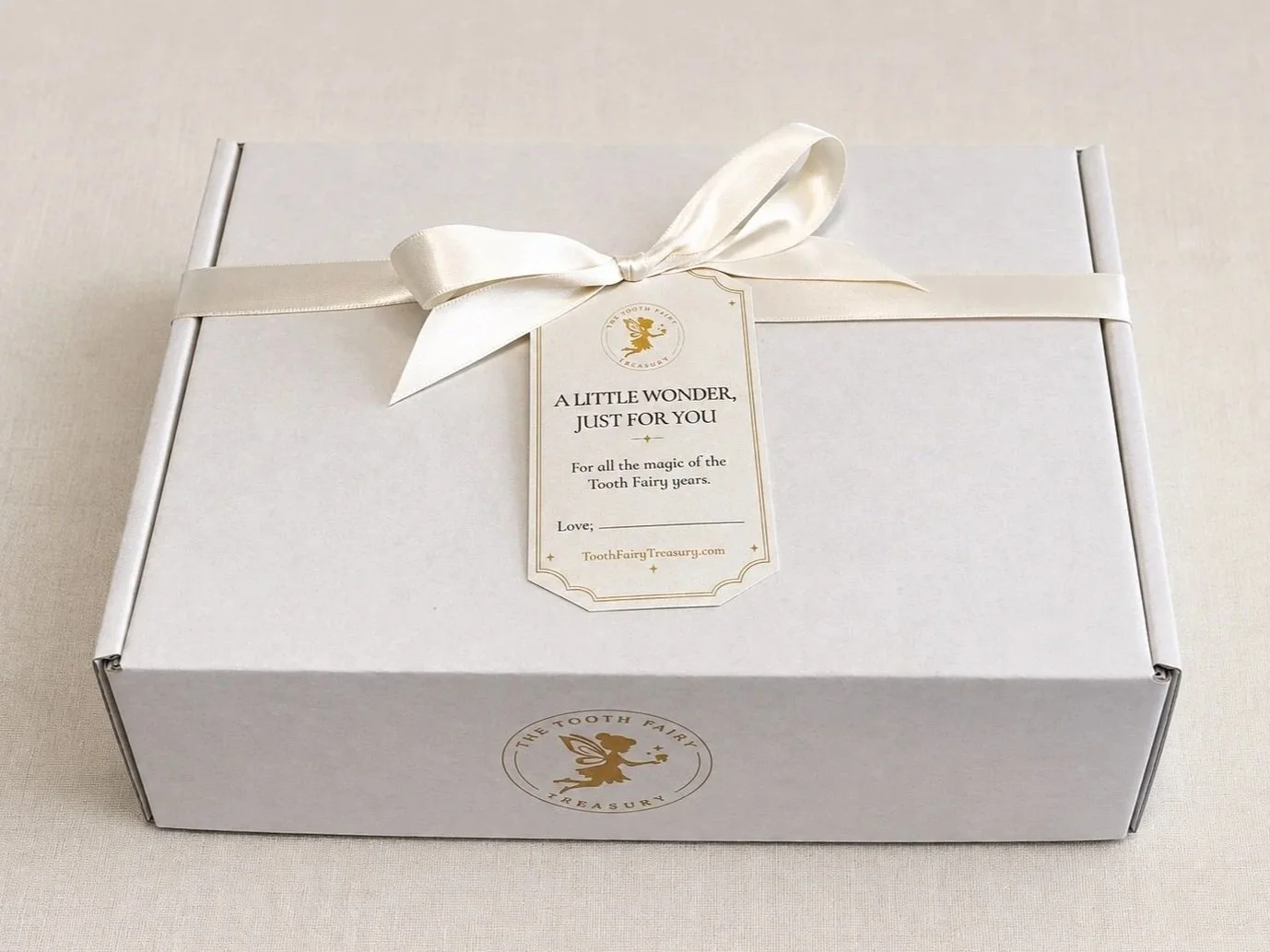 Personalized Tooth Fairy Treasury gift pack wrapped with satin ivory ribbon and gift tag, with keepsake box, tooth pouch, stationery, and Tooth Fairy booklet inside.