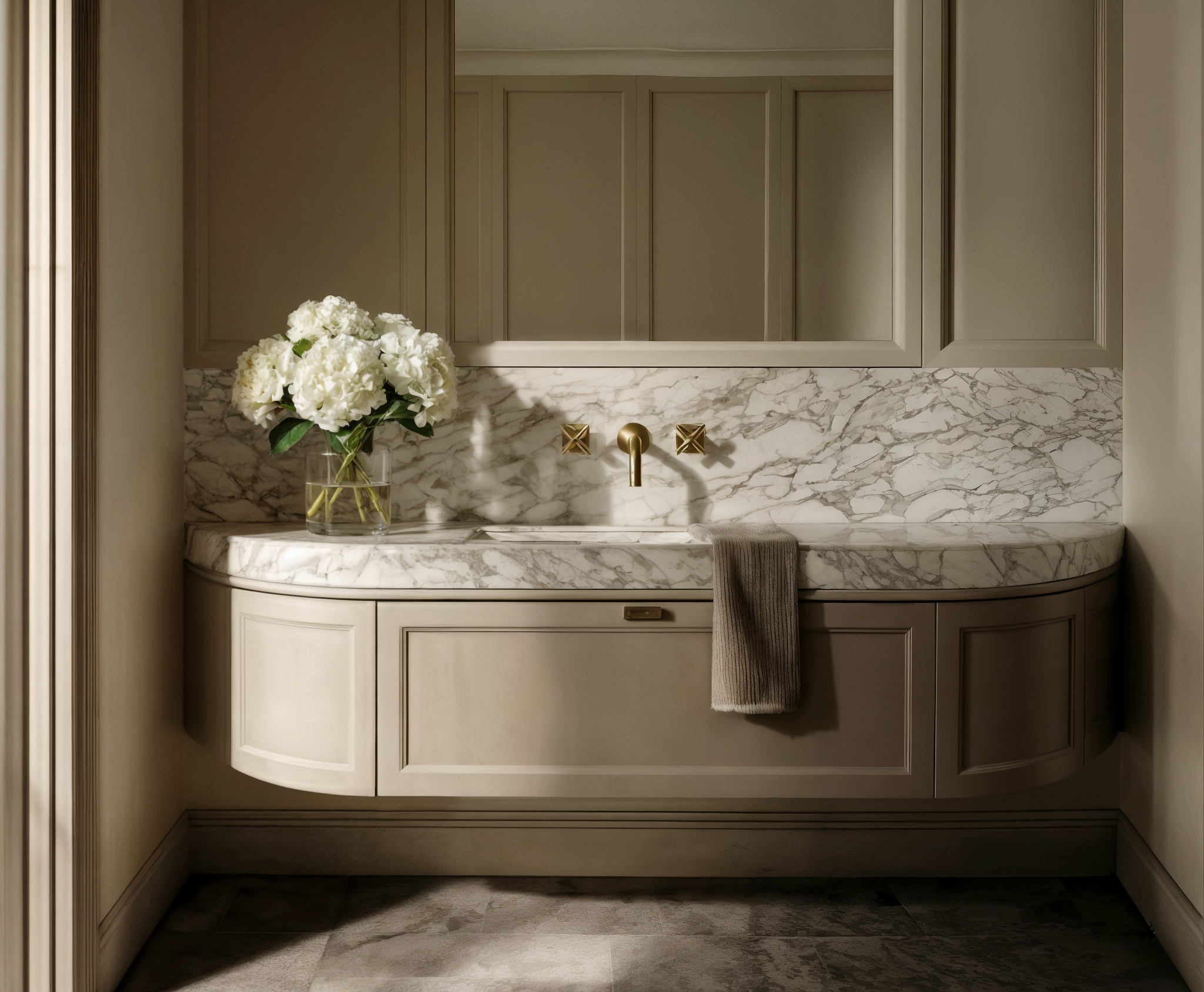Elegant curved bathroom vanity painted in taupe with a marble countertop, brass wall-mounted taps, and hydrangea styling.