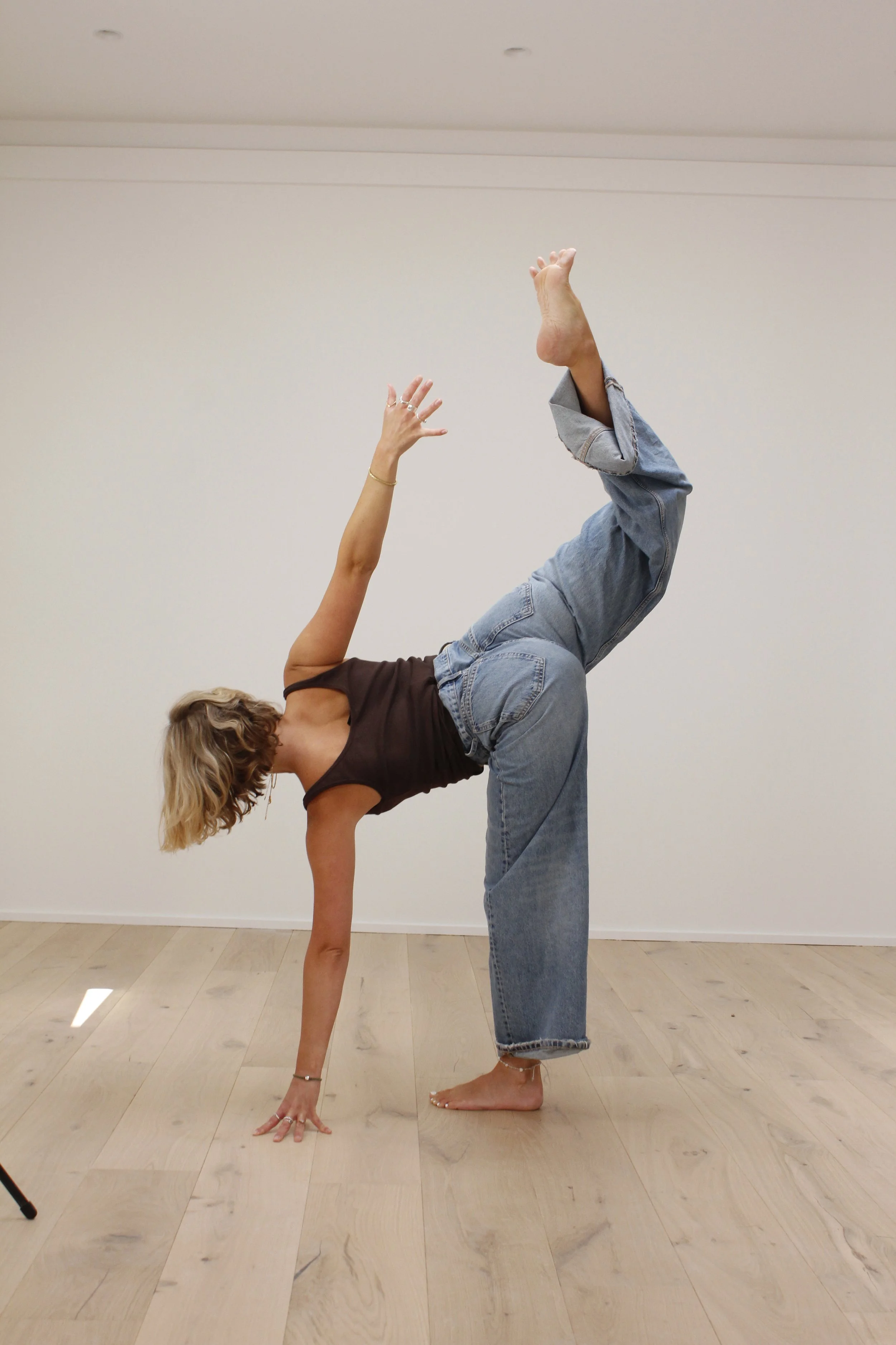 A person doing a handstand with another person balancing on their back in a yoga pose indoors against a plain white wall.