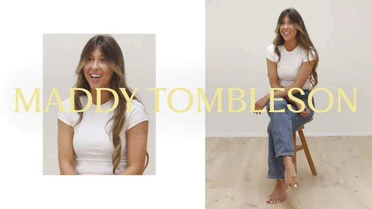 Photo of a woman with long wavy hair wearing a white top and blue jeans, sitting barefoot on a wooden stool against a plain white wall. The text 'MADDY TOMLSON' is overlaid in yellow on the image.