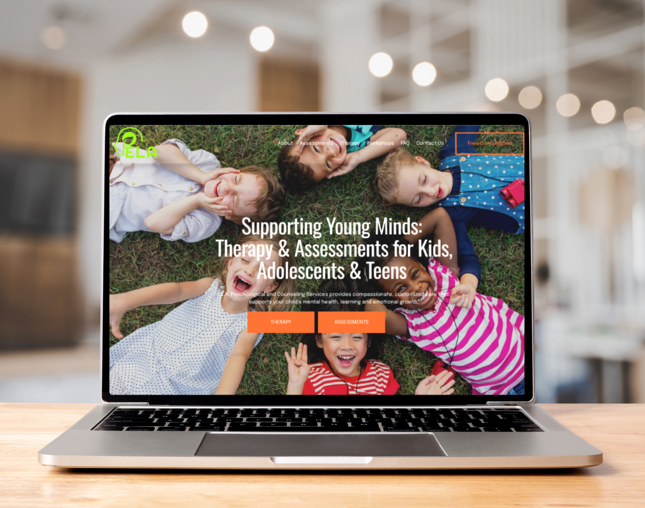 Laptop on a wooden table displaying a website with children lying on grass, smiling and laughing, with text about therapy and assessments for kids, adolescents, and teens.