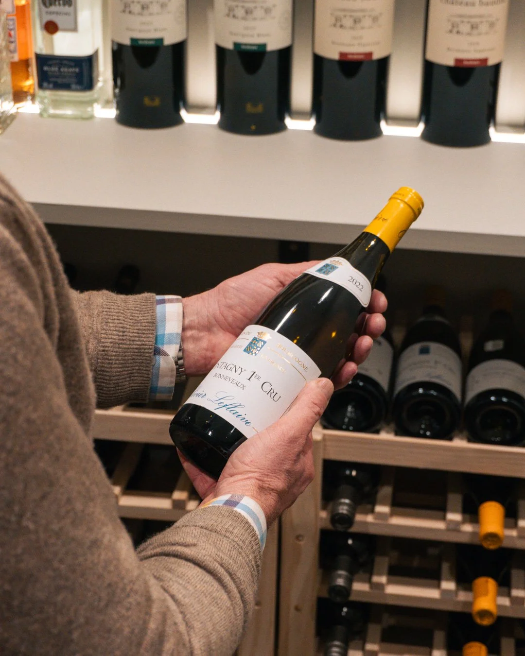 Person holding a bottle of white wine in a wine store aisle, with shelves of wine bottles in the background.