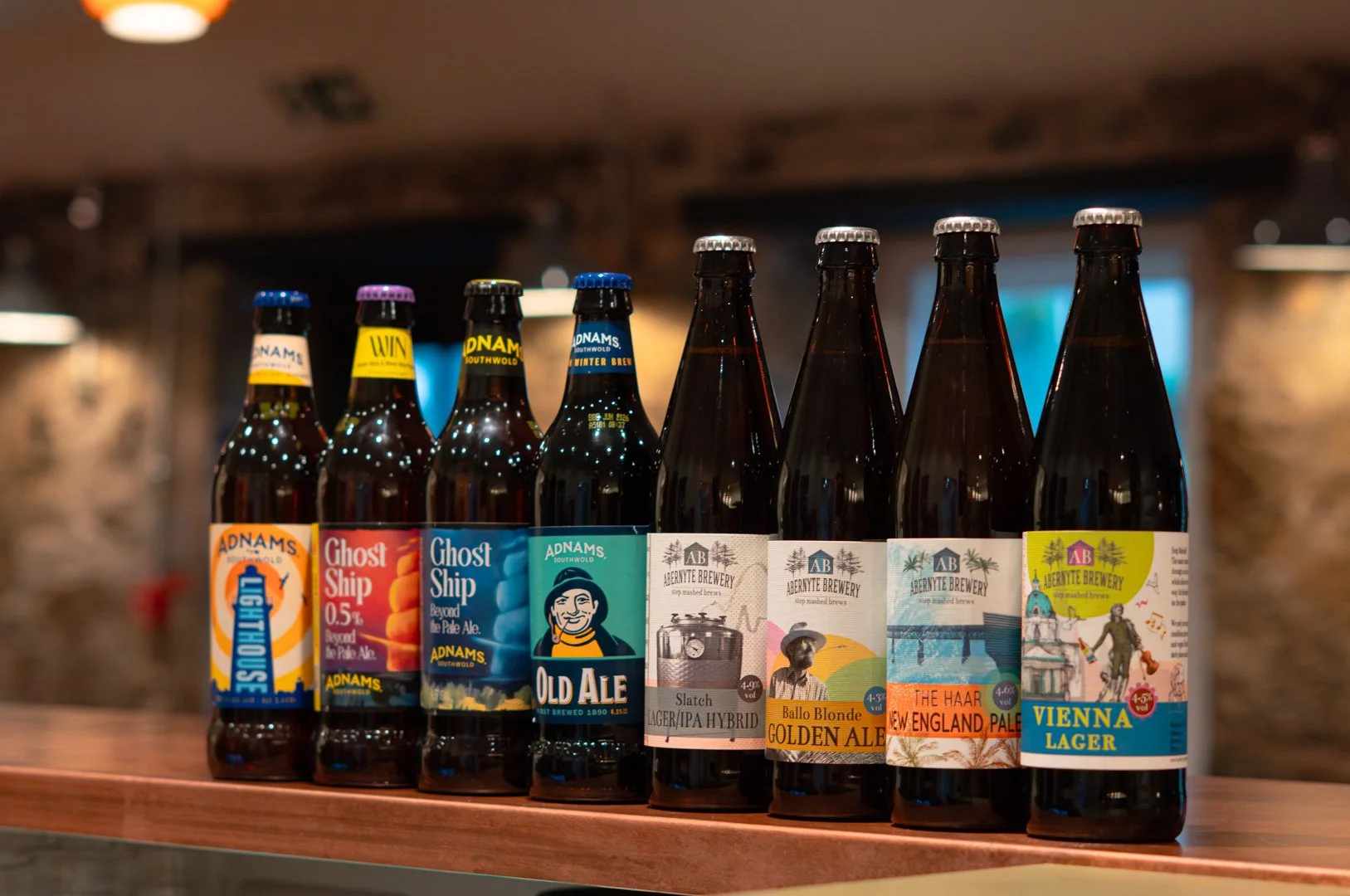A row of craft beer bottles on a wooden surface, with colorful labels from various breweries.