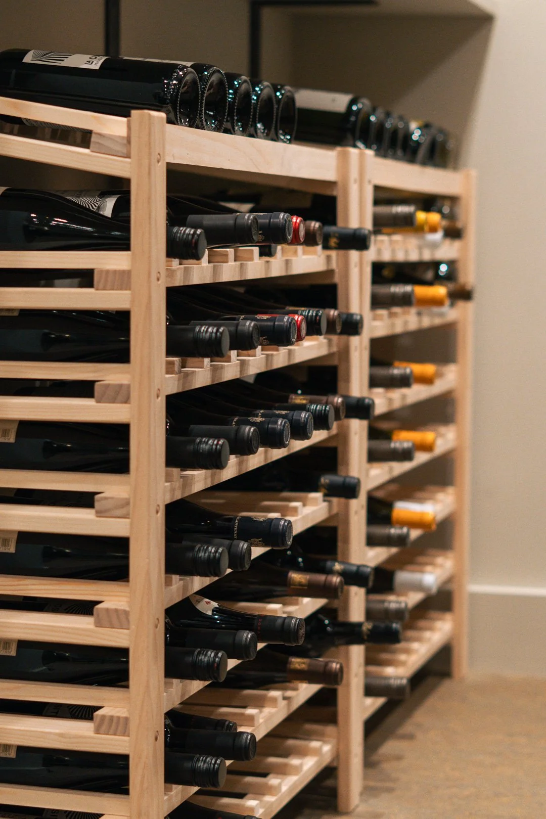 Multiple wine bottles stored on wooden racks in a wine cellar or storage closet.