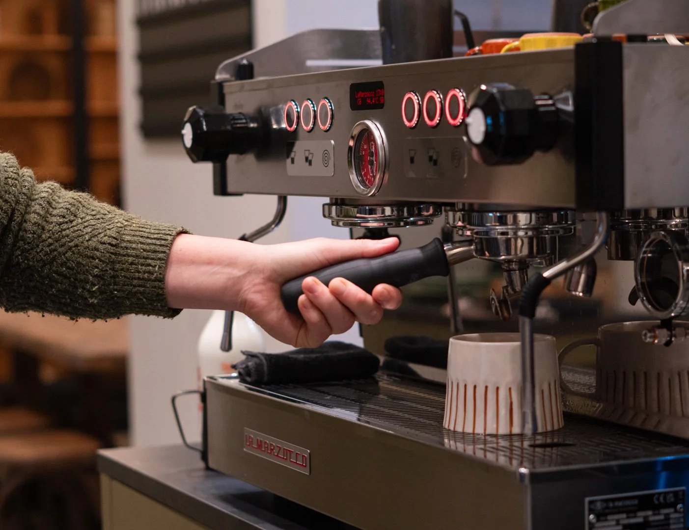 A person using a commercial espresso machine to make coffee in a cafe.
