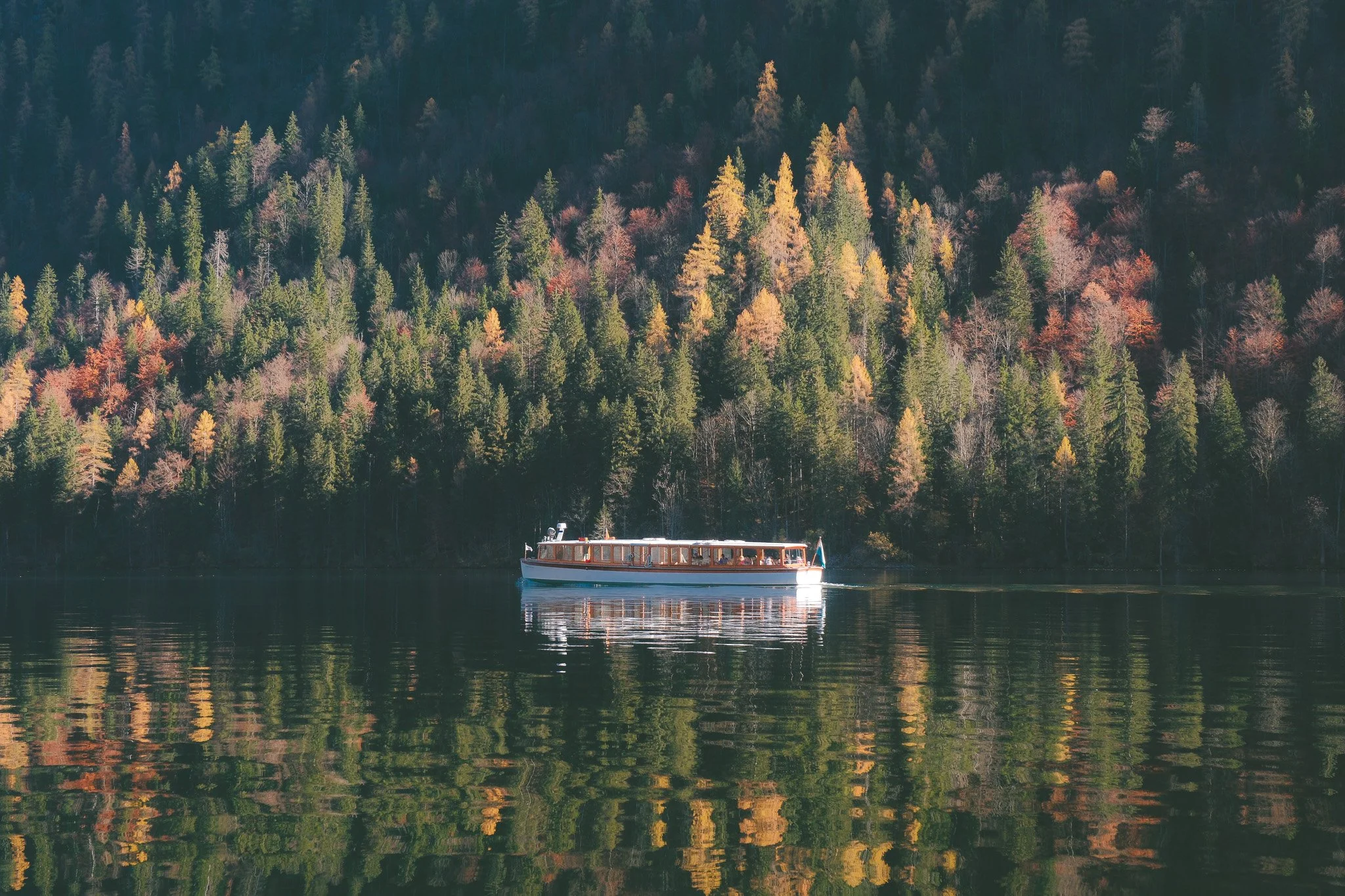 A boat on a calm lake with a forested hillside in the background, featuring trees with fall colors.